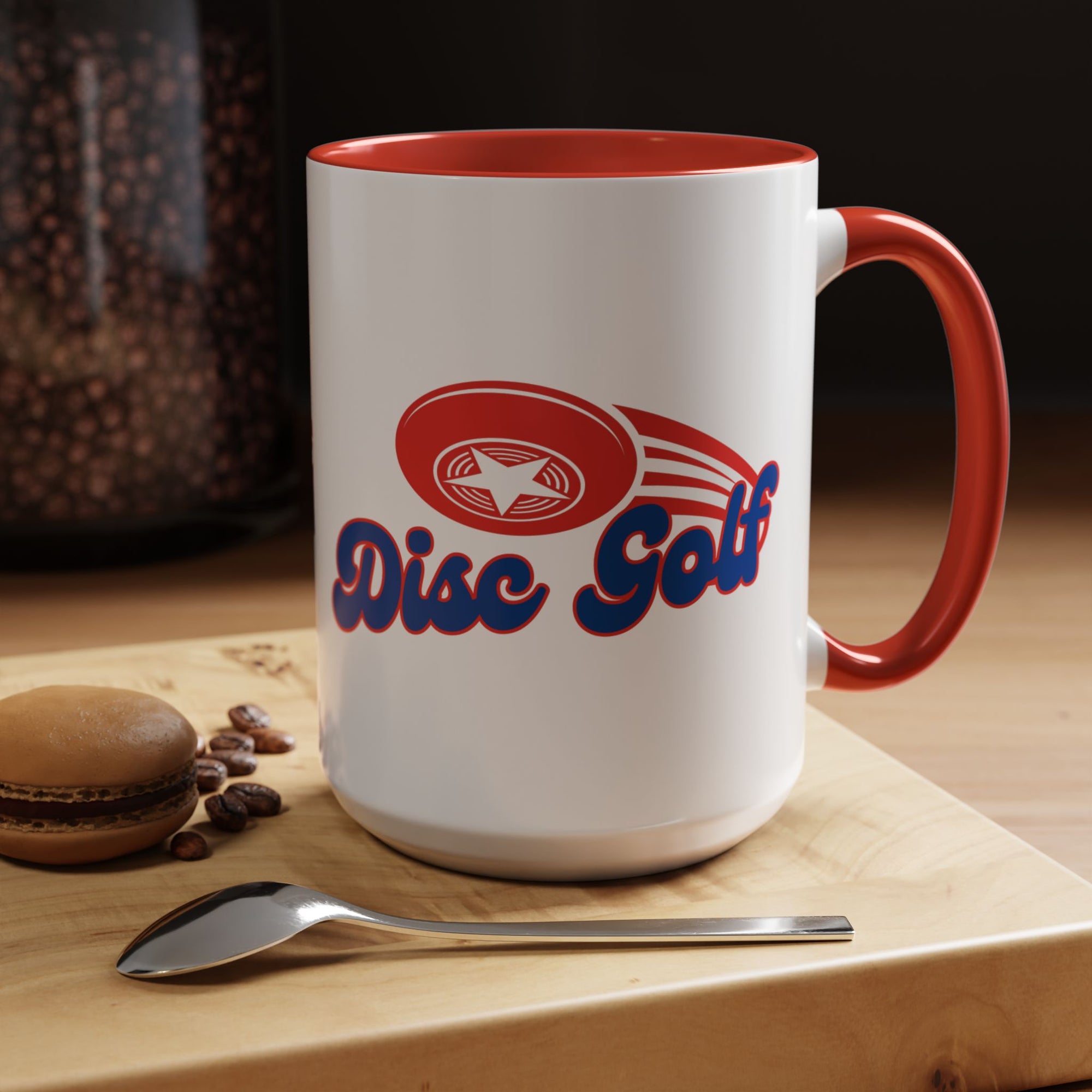 A ceramic coffee mug with red accents on the handle and interior, with 'Disc Golf' in a blue script text outlined in red and disc golf with motion trails, in a coffee shop setting