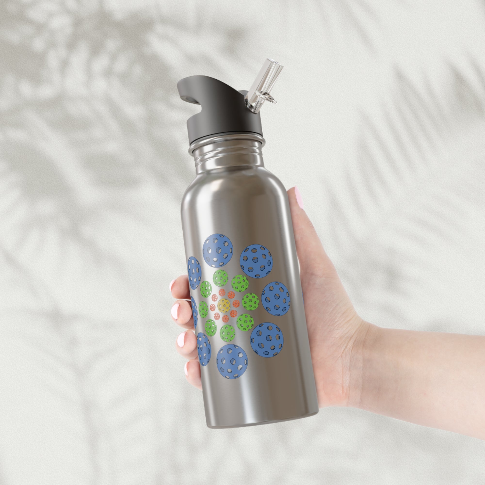 A hand holding a stainless steel water bottle with lid featuring a colorful geometric design of pickleballs against a white background