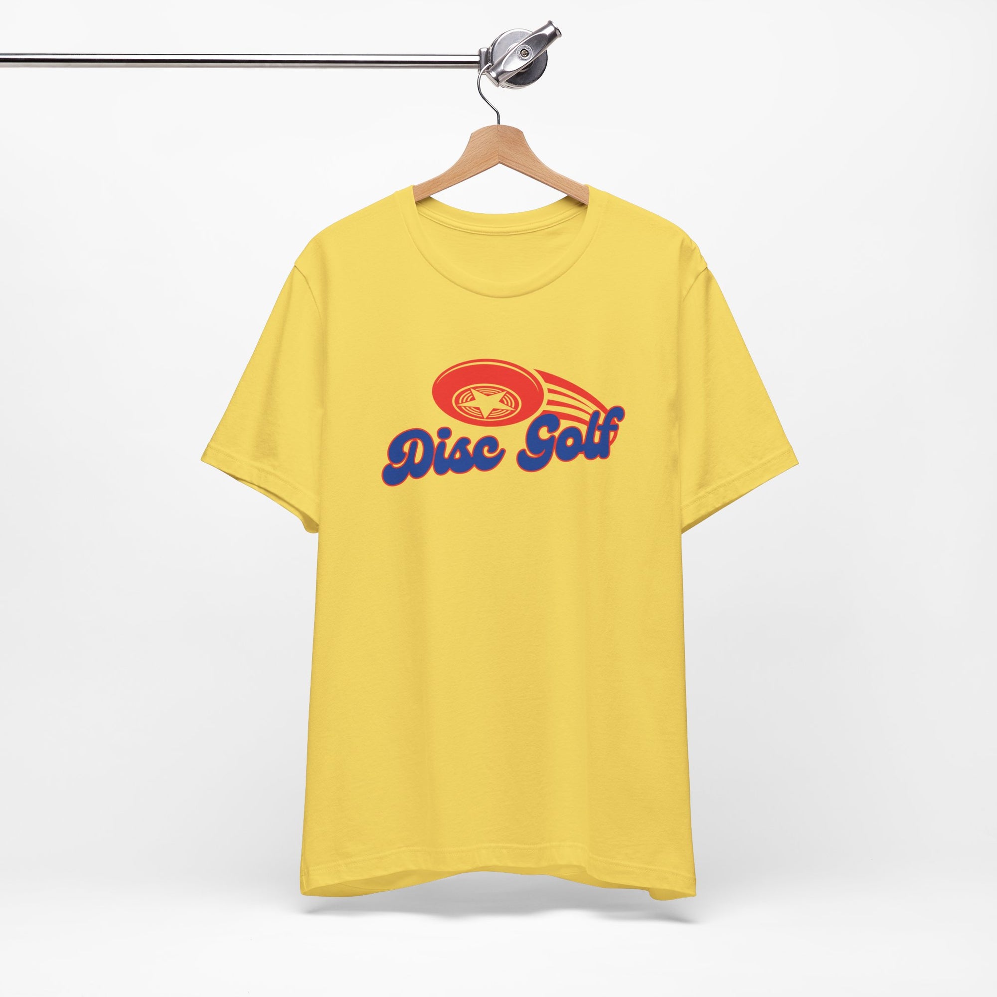 Yellow t-shirt with 'Disc Golf' in a blue script text outlined in red and disc golf with motion trails, on a hanger against a white background