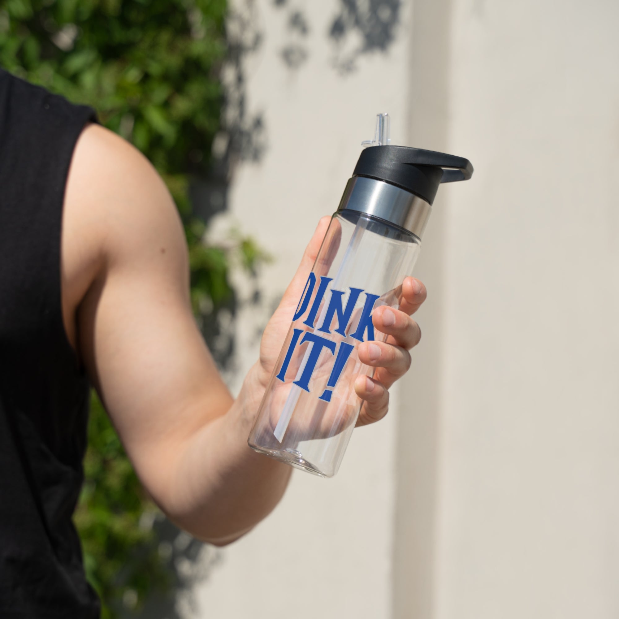 A man holding a clear water bottle with lid featuring the words 'DINK IT!' text in blue and outlined in gray, against a white background
