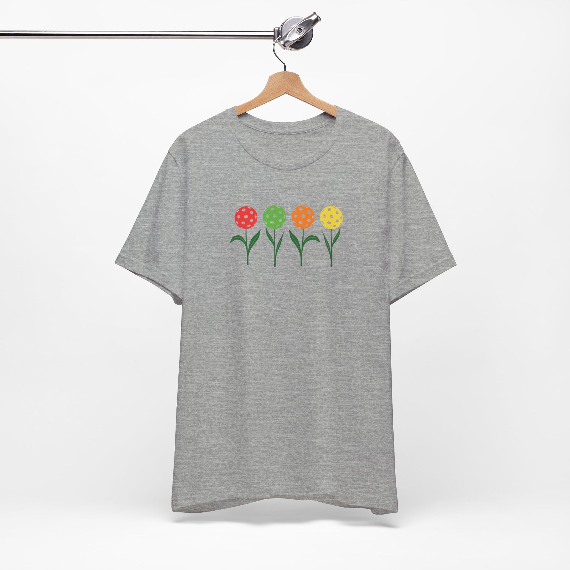 Light gray t-shirt with colorful flowers made from pickleballs on green stems with leaves, on a hanger against a white background