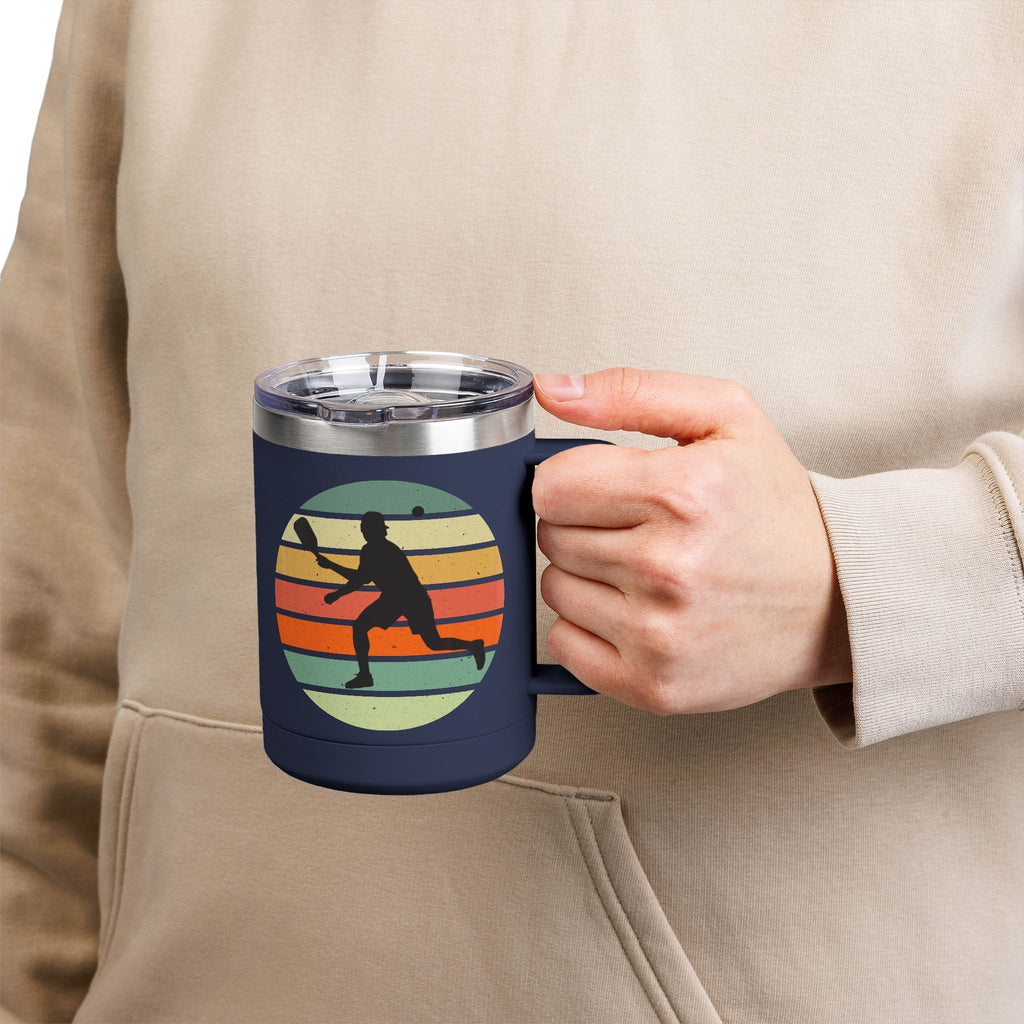 Person holding a blue mug with a graphic of a person's silhouette playing pickleball on a retro color background