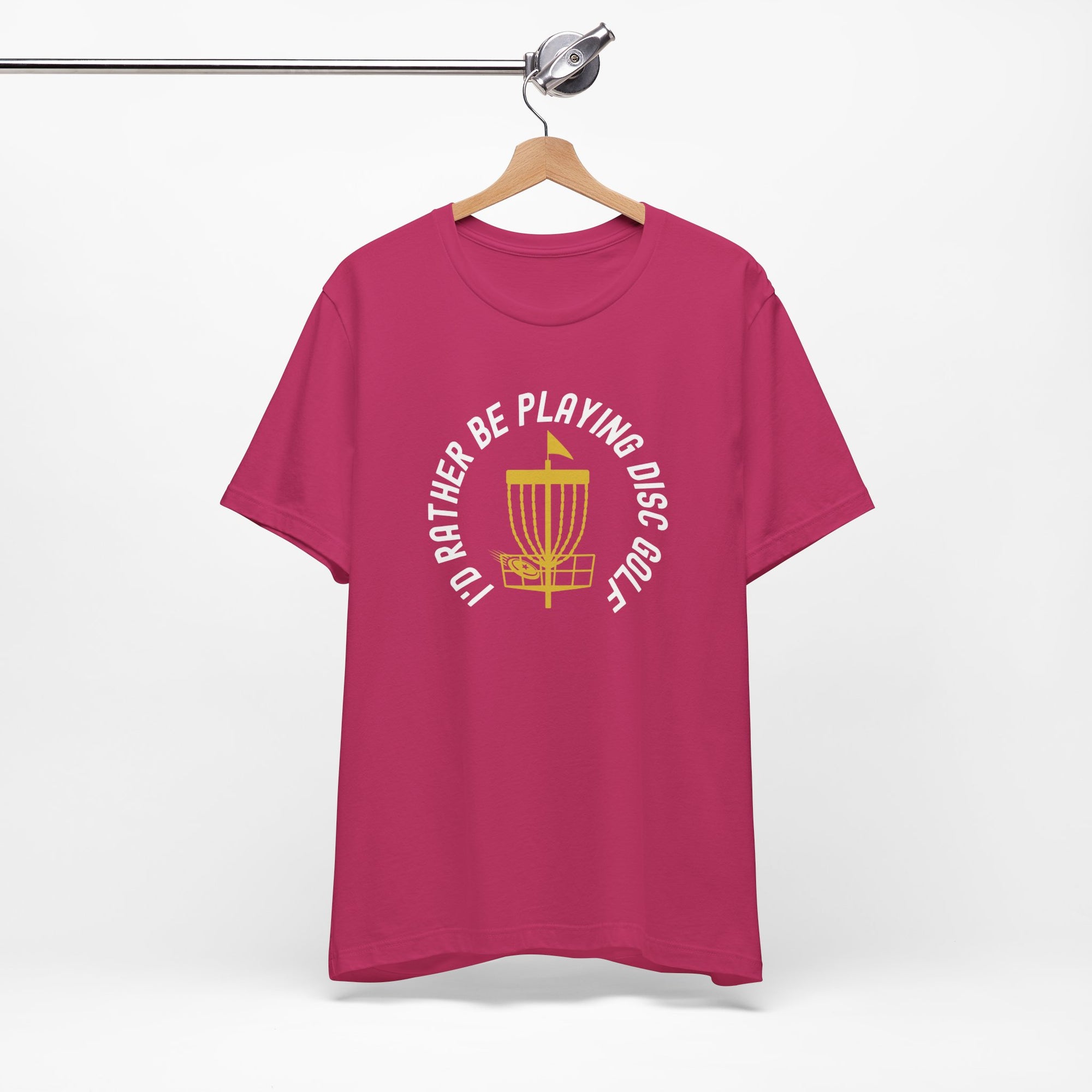 Pink t-shirt with a graphic of disc golf chains, basket, and disc and text that says "I'd Rather Be Playing Disc Golf" on a hanger against a white background