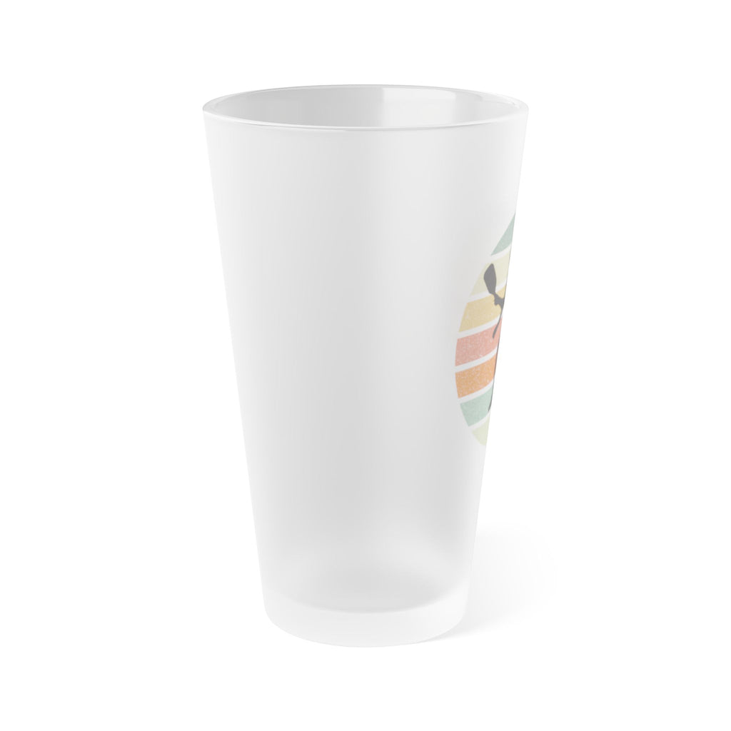 Side view of a frosted pint glass with a silhouette of a pickleball player over a circle of colorful lines, on a white background