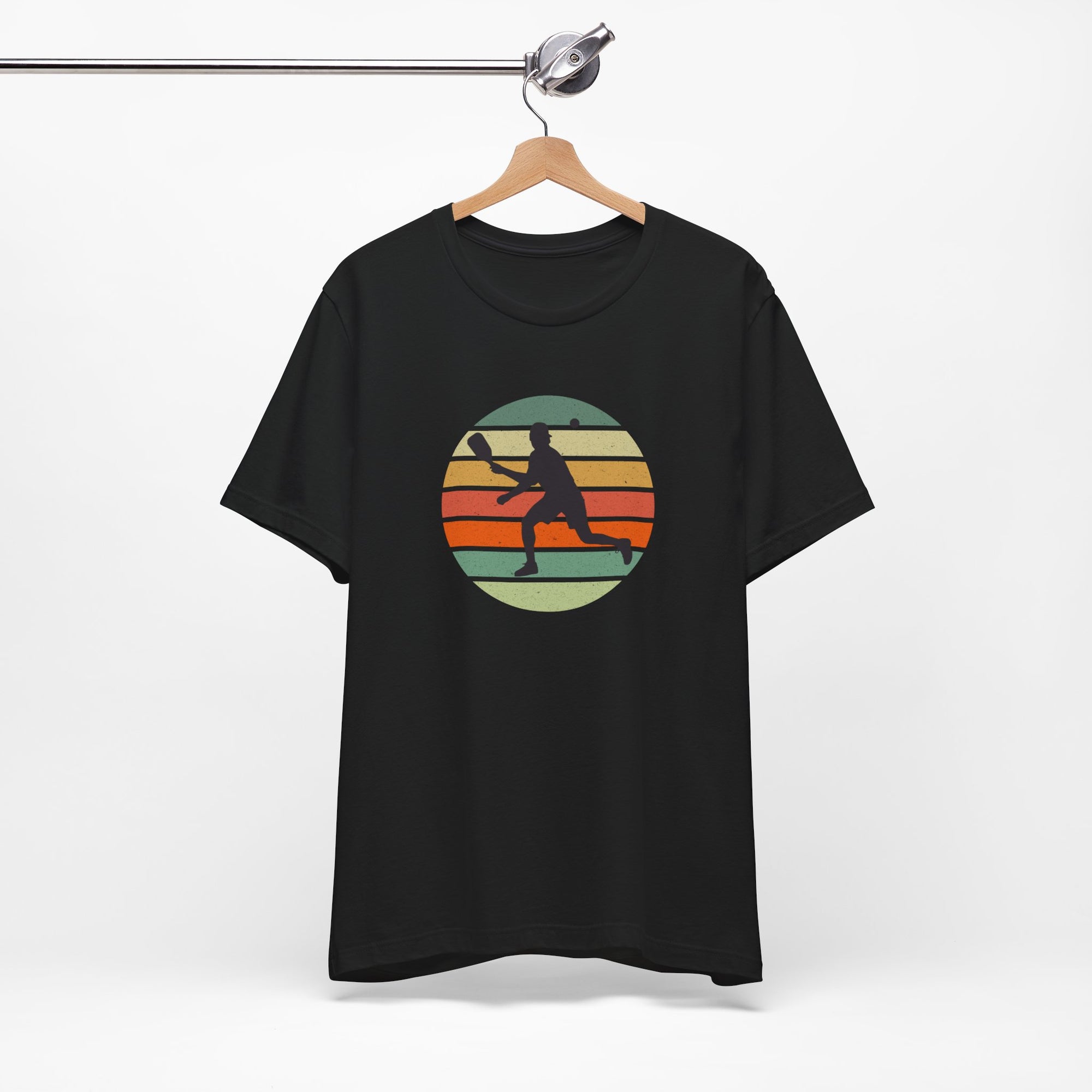 Black t-shirt with a colorful graphic of a person playing pickleball on a hanger against a white background