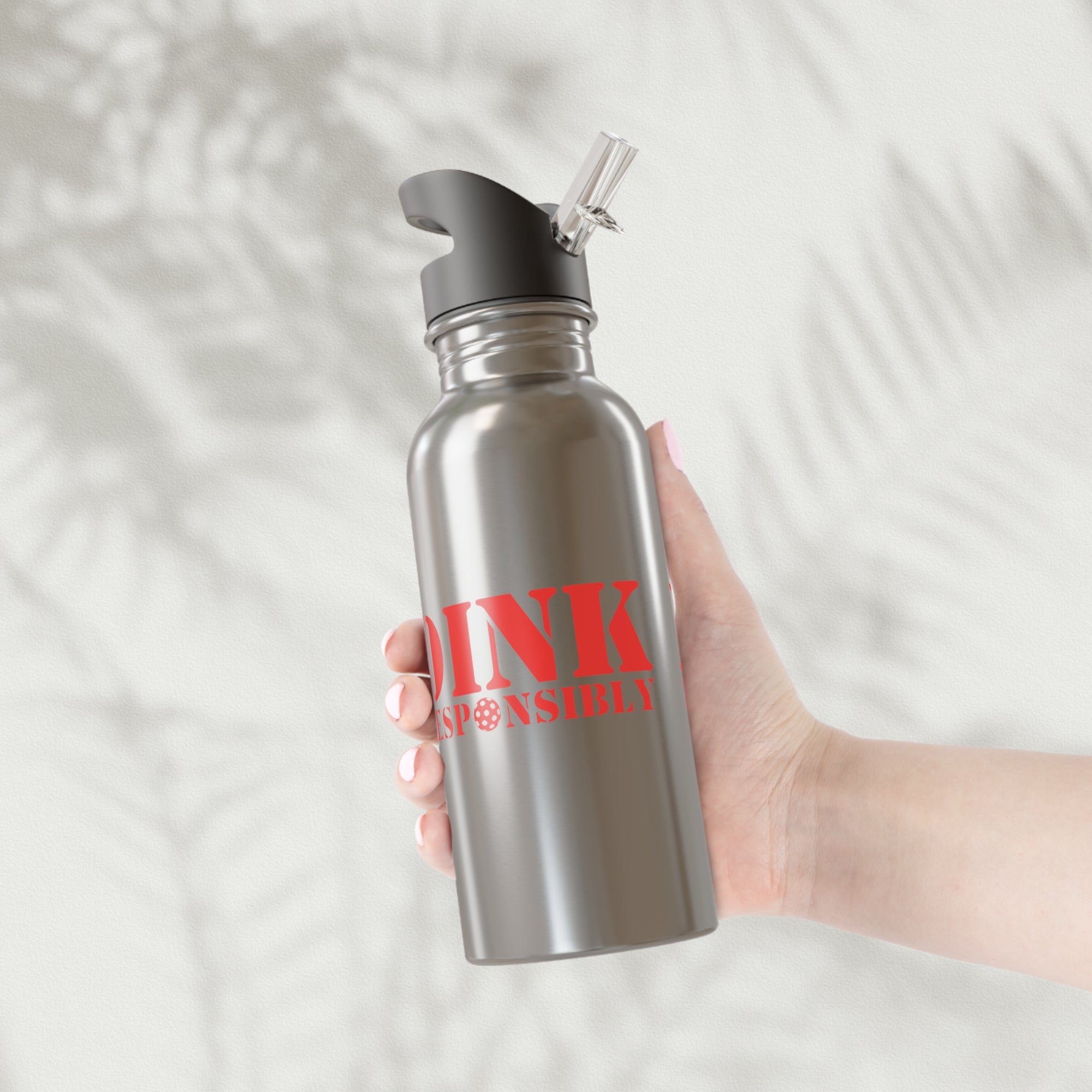 A hand holding a stainless steel water bottle with red text 'DINK RESPONSIBLY' with a pickleball replacing the "O" in "Responsibly" against a white background