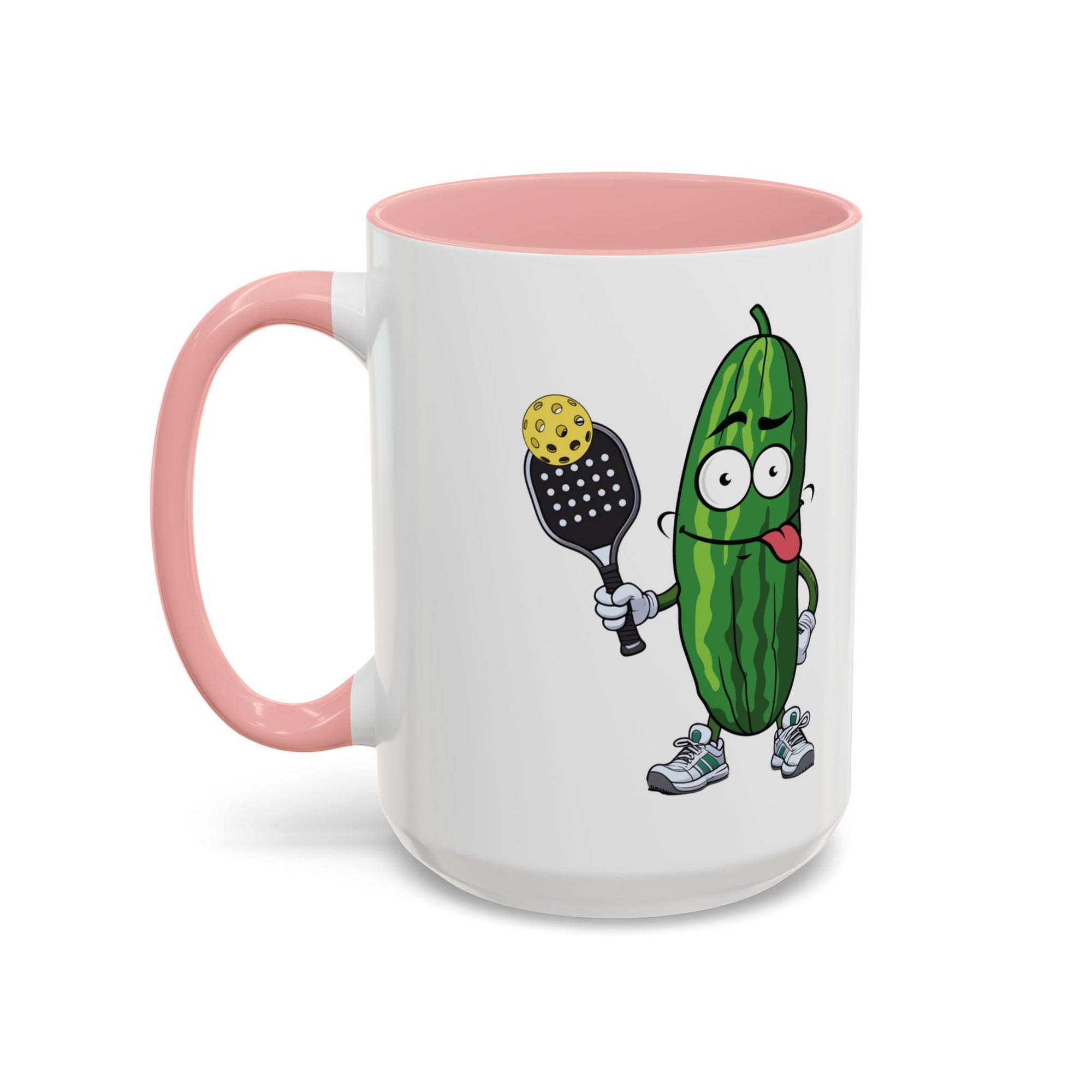 A ceramic coffee mug with pink accents on the handle and interior, with a cartoon pickle with googly eyes and his tongue sticking out, holding a pickleball paddle with a yellow pickleball, against a white background