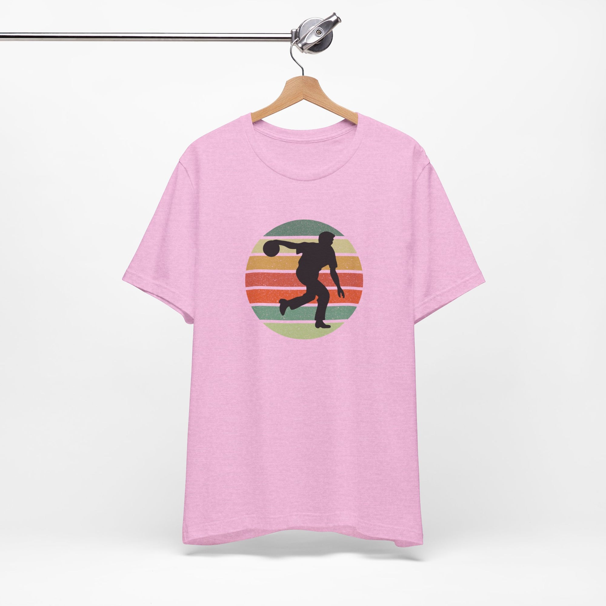 Pink t-shirt with a graphic of a silhouette of a bowler over a colorful retro image, hanging on a wooden hanger against a white background.