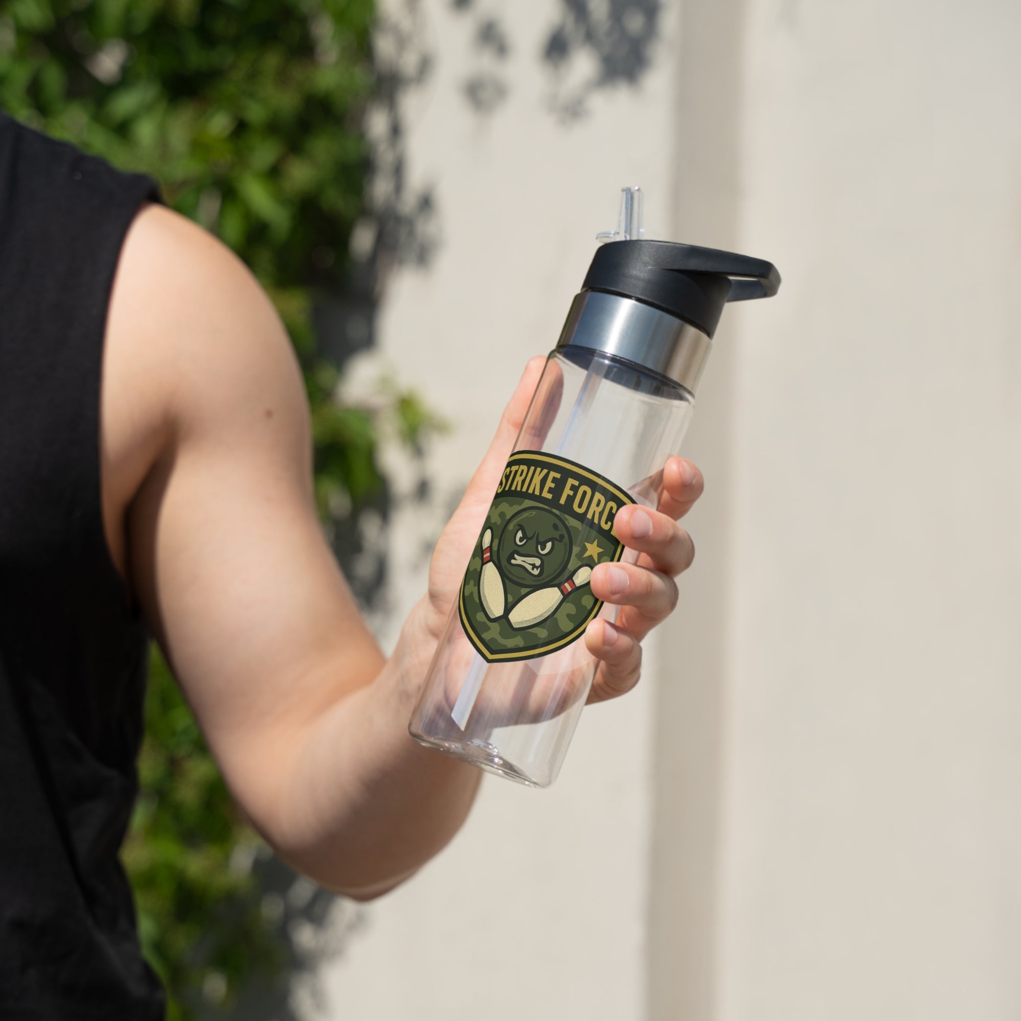 A person holding a clear water bottle with black lid, with bowling 'Strike Force' military-style patch