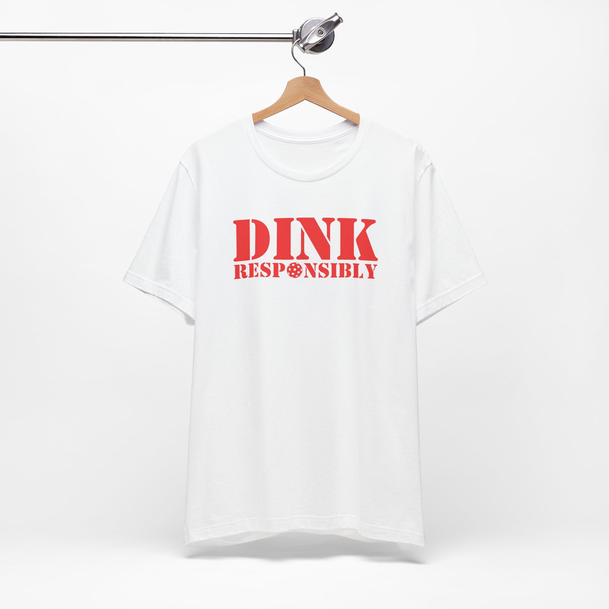 White t-shirt with red text 'DINK RESPONSIBLY' with a pickleball replacing the "O" in "Responsibly" on a hanger against a white background