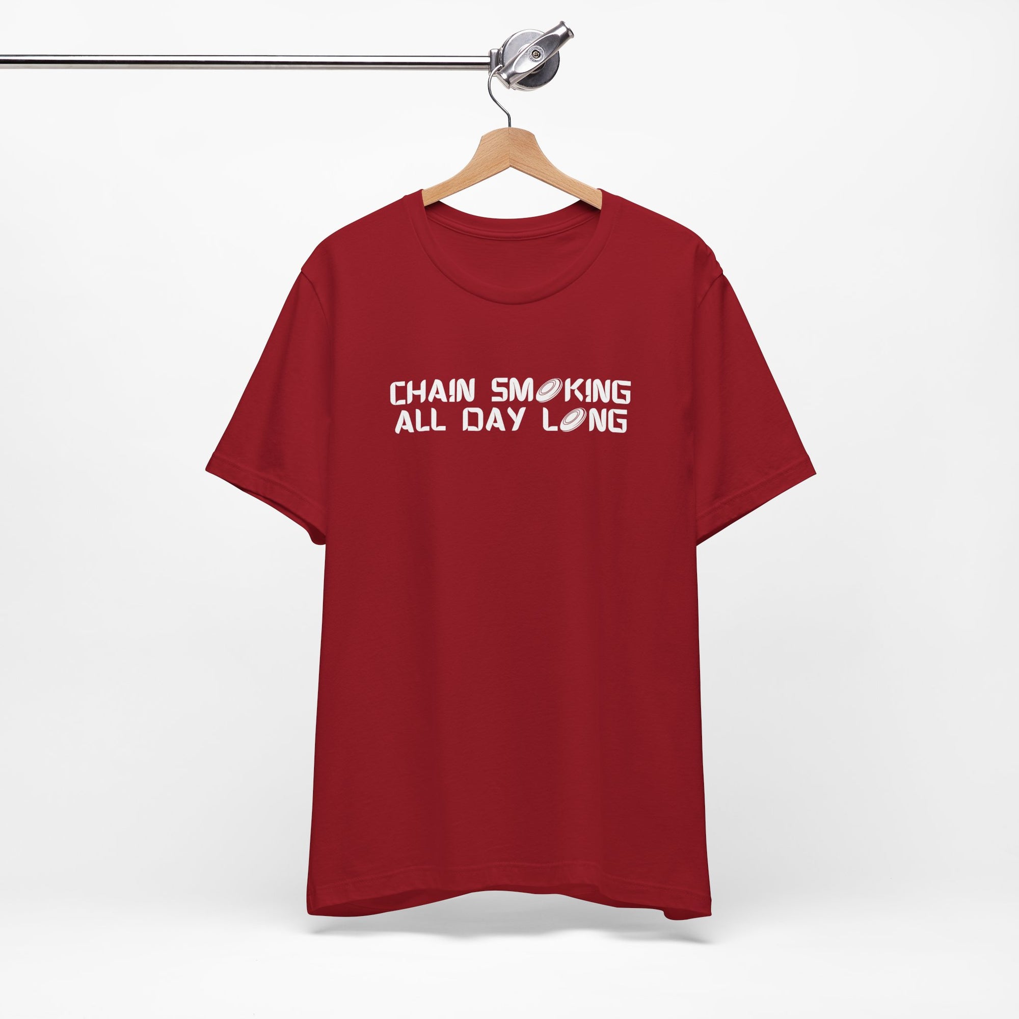 Red t-shirt with 'CHAIN SMOKING ALL DAY LONG' text with the O's replaced by disc golf discs, on a hanger against a white background