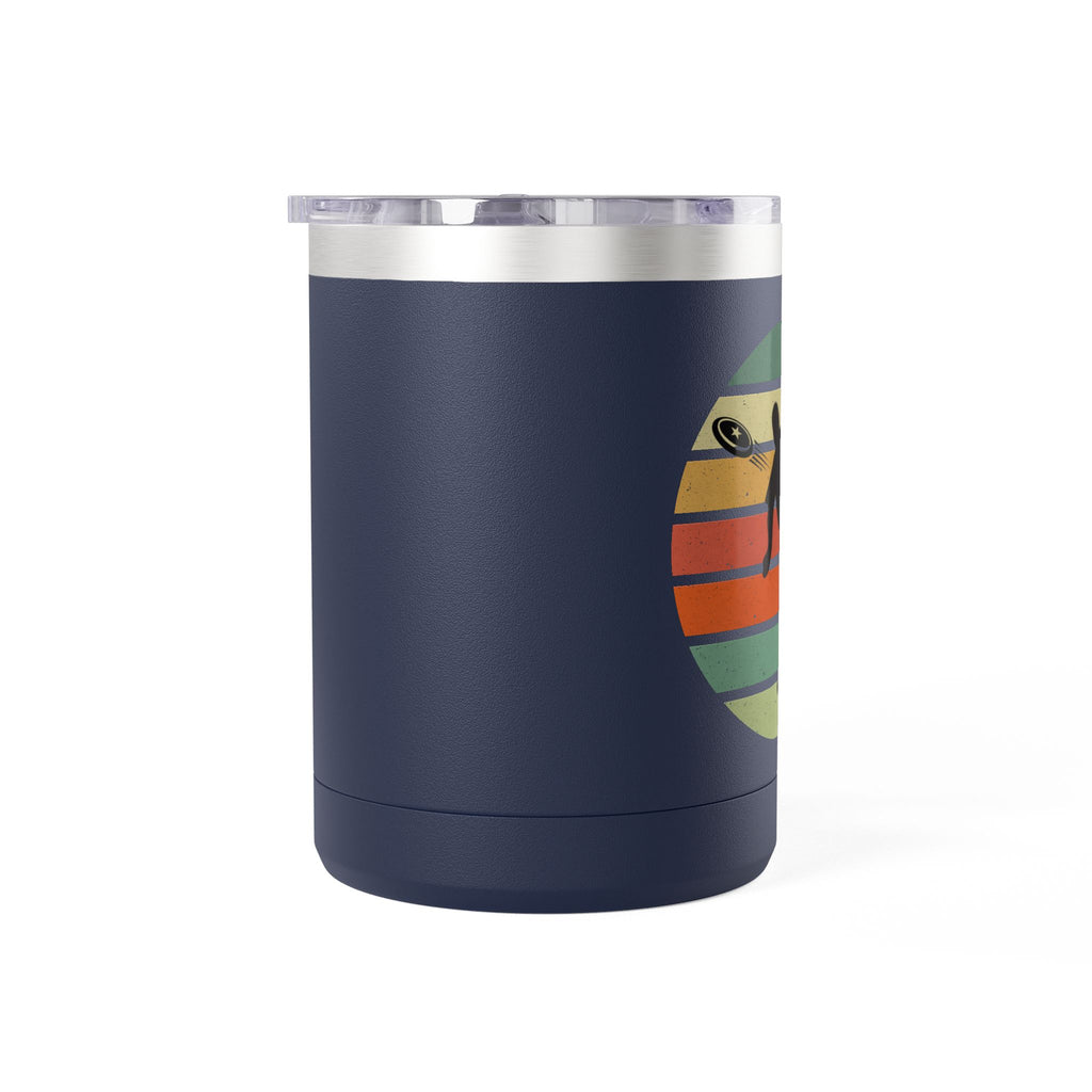Side view of a blue stainless steel coffee tumbler with handle and lid and a design on one side featuring a silhouette of a person playing disc golf over a colorful retro image, on a white background.