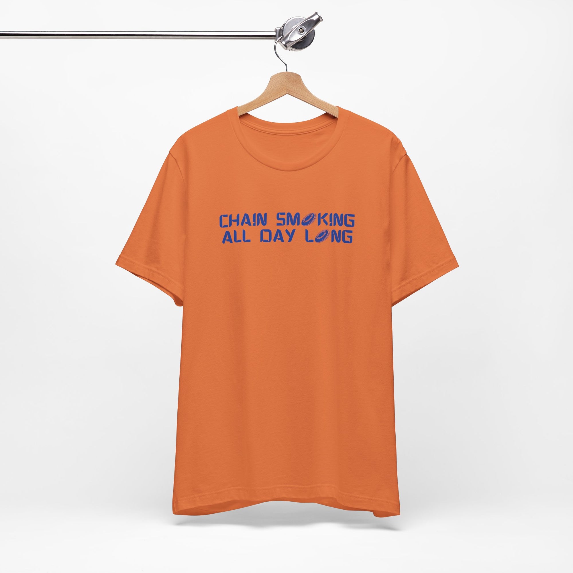 Orange t-shirt with 'CHAIN SMOKING ALL DAY LONG' text with the O's replaced by disc golf discs, on a hanger against a white background