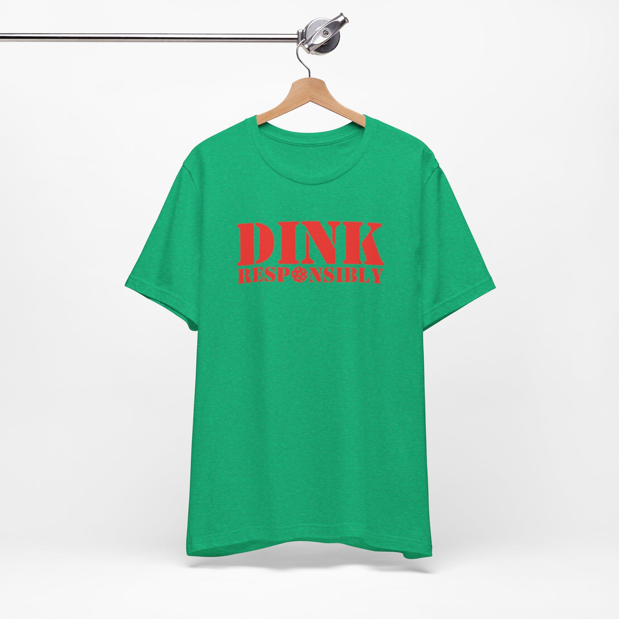 Green t-shirt with red text 'DINK RESPONSIBLY' with a pickleball replacing the "O" in "Responsibly" on a hanger against a white background