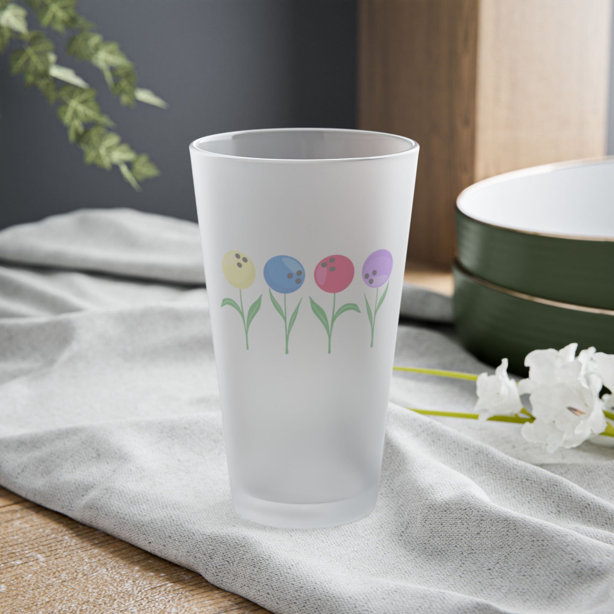A frosted pint glass with colorful flowers made out of bowling balls, on a tabletop
