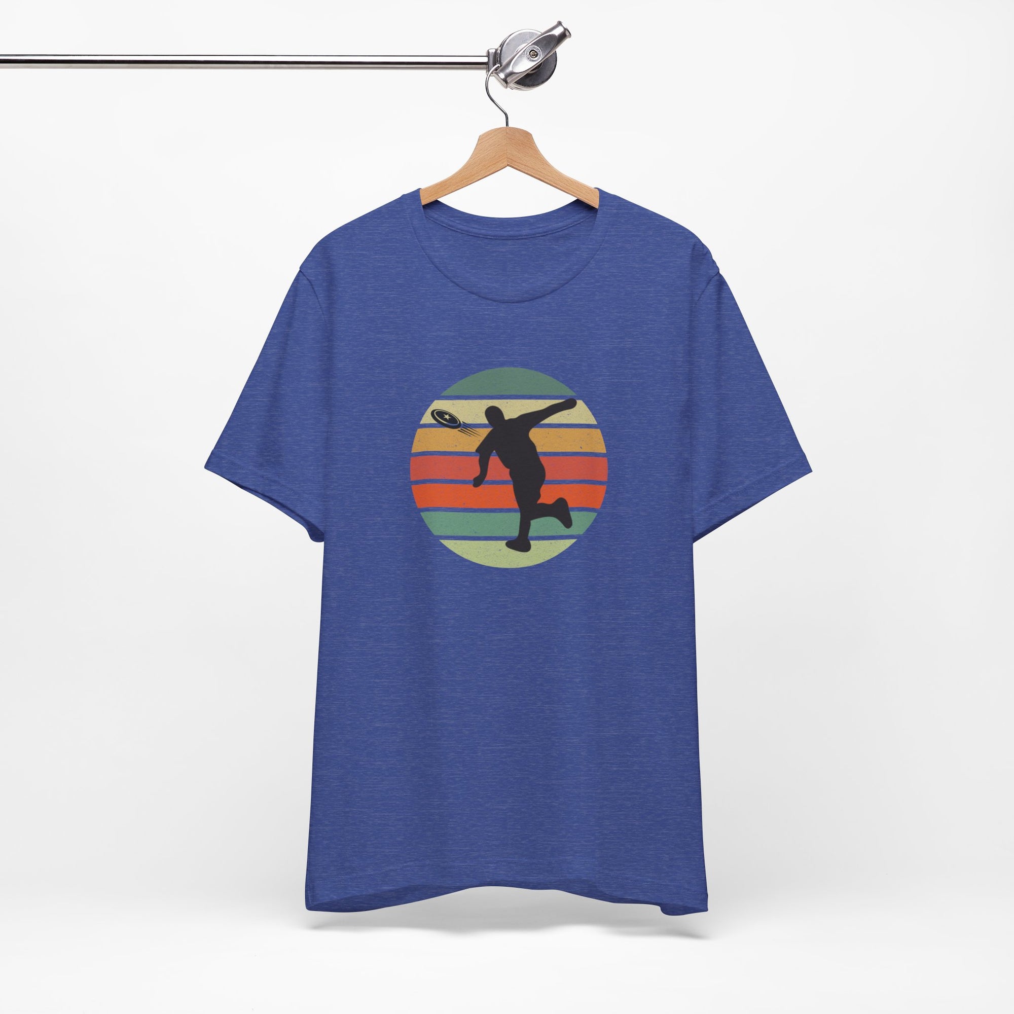 Blue t-shirt with a graphic of a silhouette disc golf player throwing a disc above a colorful retro graphic, hanging on a wooden hanger.