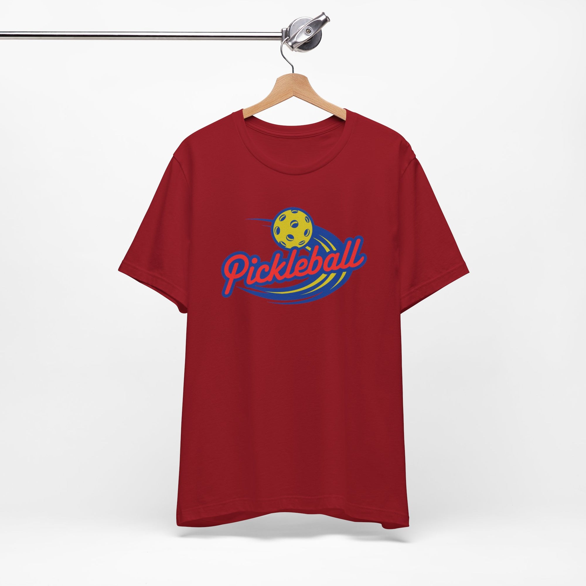 Maroon t-shirt with a classic pickleball logo featuring the word pickleball and a yellow pickleball with motion lines, on a hanger against a white background