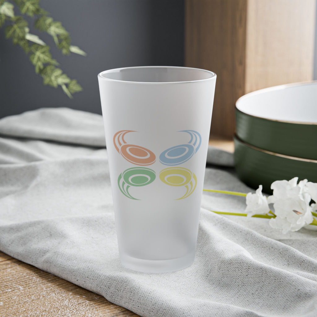 A frosted pint glass with four colorful disc golf disc with motion trails, on a tabletop