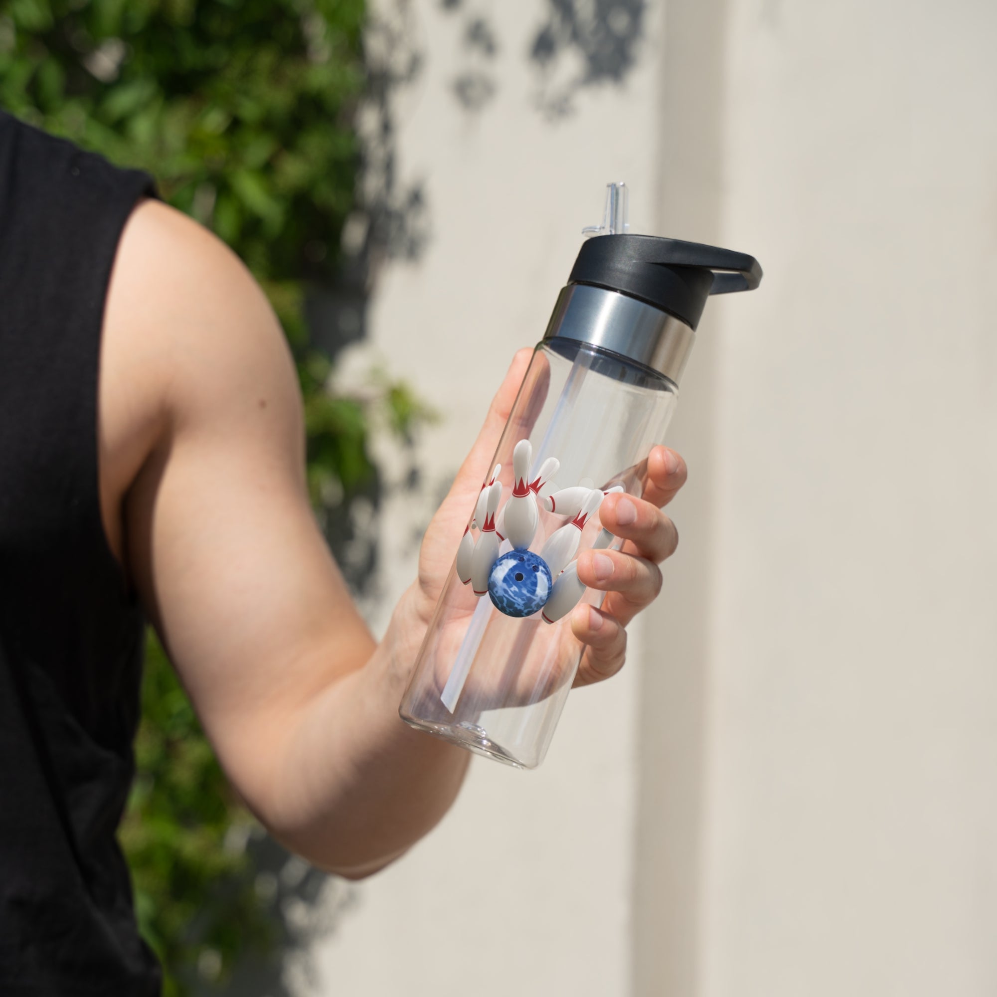 A person holding a clear water bottle with black lid, with a graphic of a blue bowling ball knocking over bowling pins