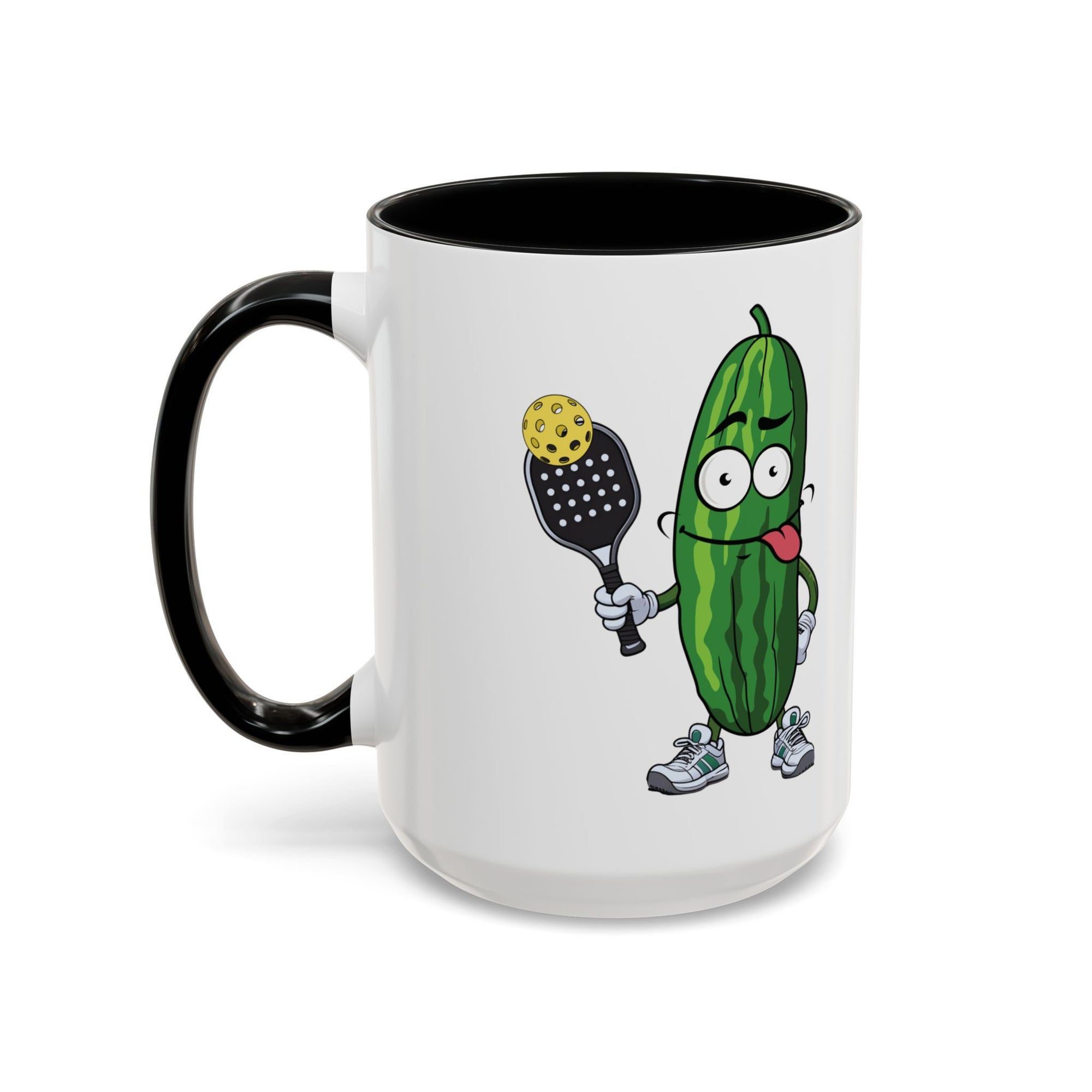A ceramic coffee mug with black accents on the handle and interior, with a cartoon pickle with googly eyes and his tongue sticking out, holding a pickleball paddle with a yellow pickleball, against a white background