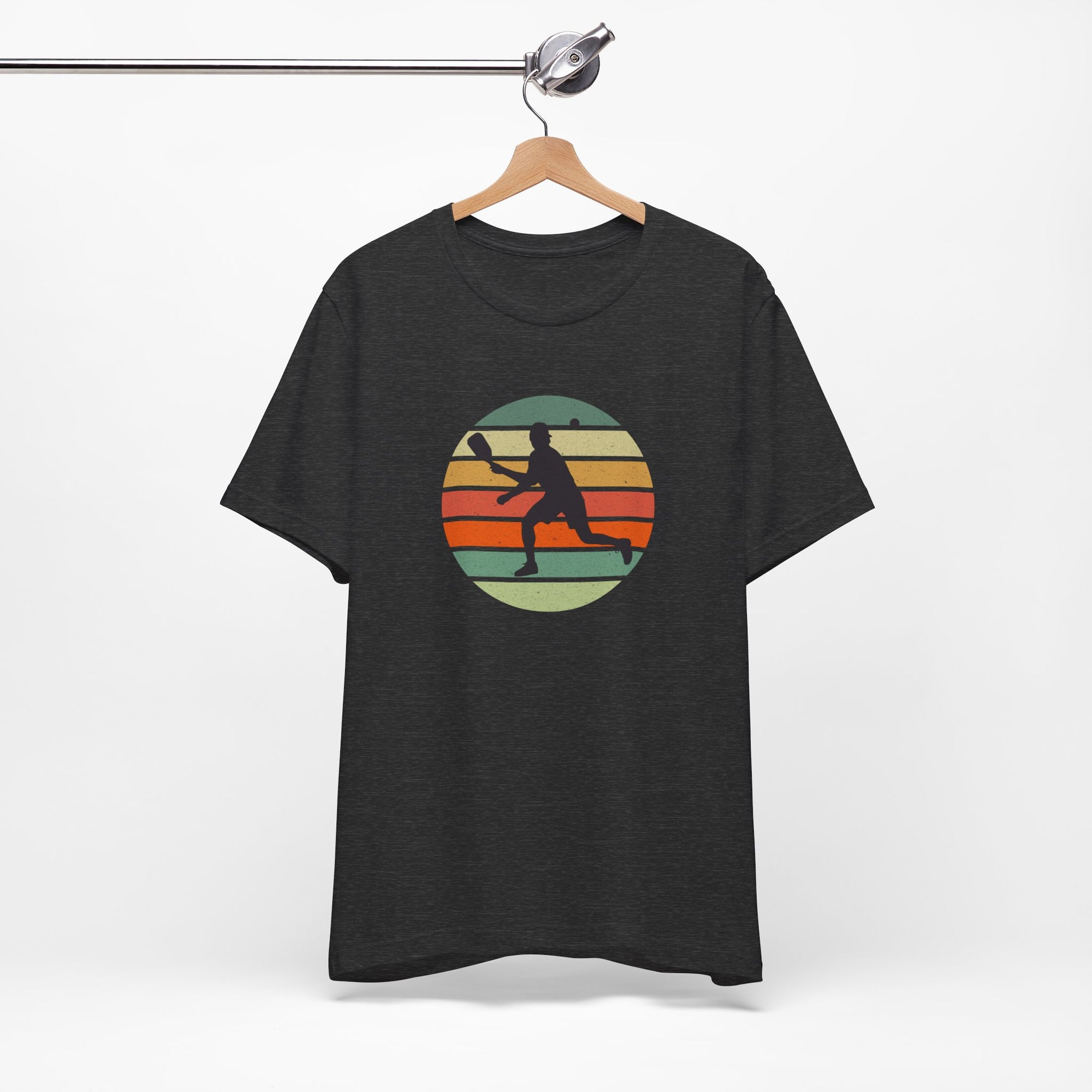 Grey t-shirt with a colorful graphic of a person playing pickleball on a hanger against a white background