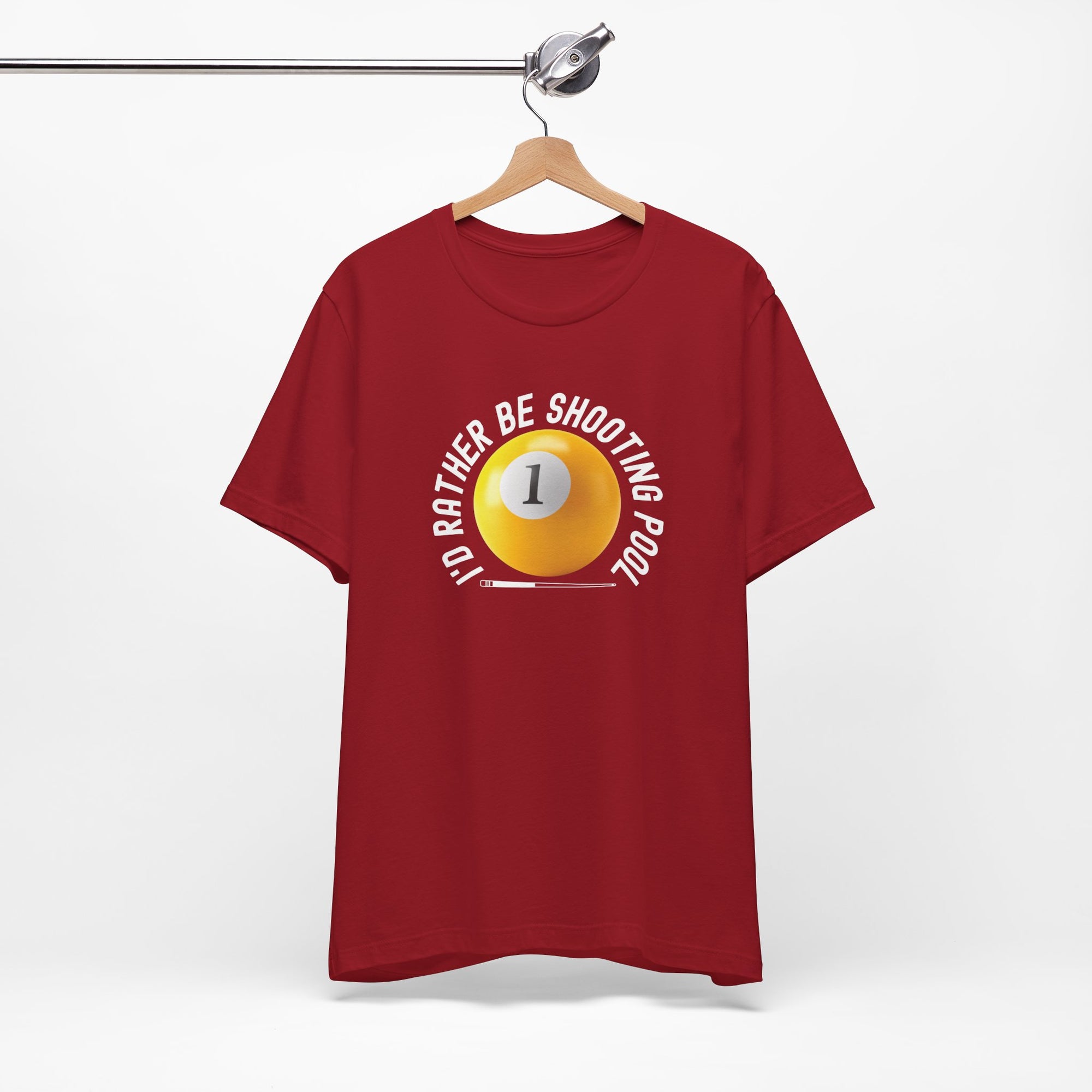 Red t-shirt with a yellow billiards ball and cue stick graphic and the text "I'd Rather Be Shooting Pool" on a hanger against a white background