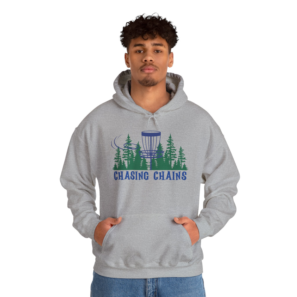 A man wearing a gray hoodie with 'Chasing Chains' graphic featuring a flying disc golf disc and basket and chains in front of a scenic evergreen tree landscape, against a white background