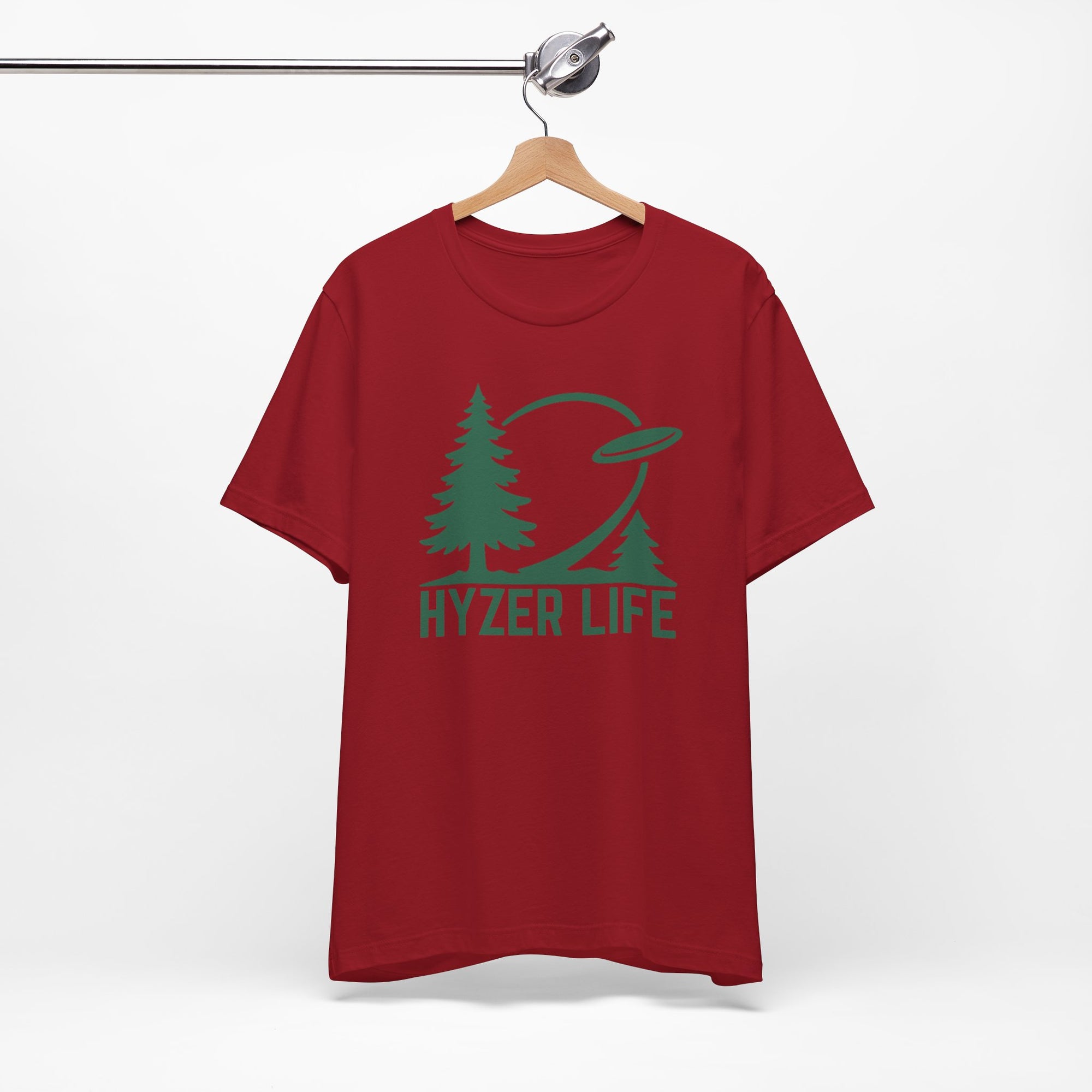 Maroon t-shirt with green graphic of trees and a disc golf flying with the words 'HYZER LIFE' below the image, on a hanger against a white backgroud