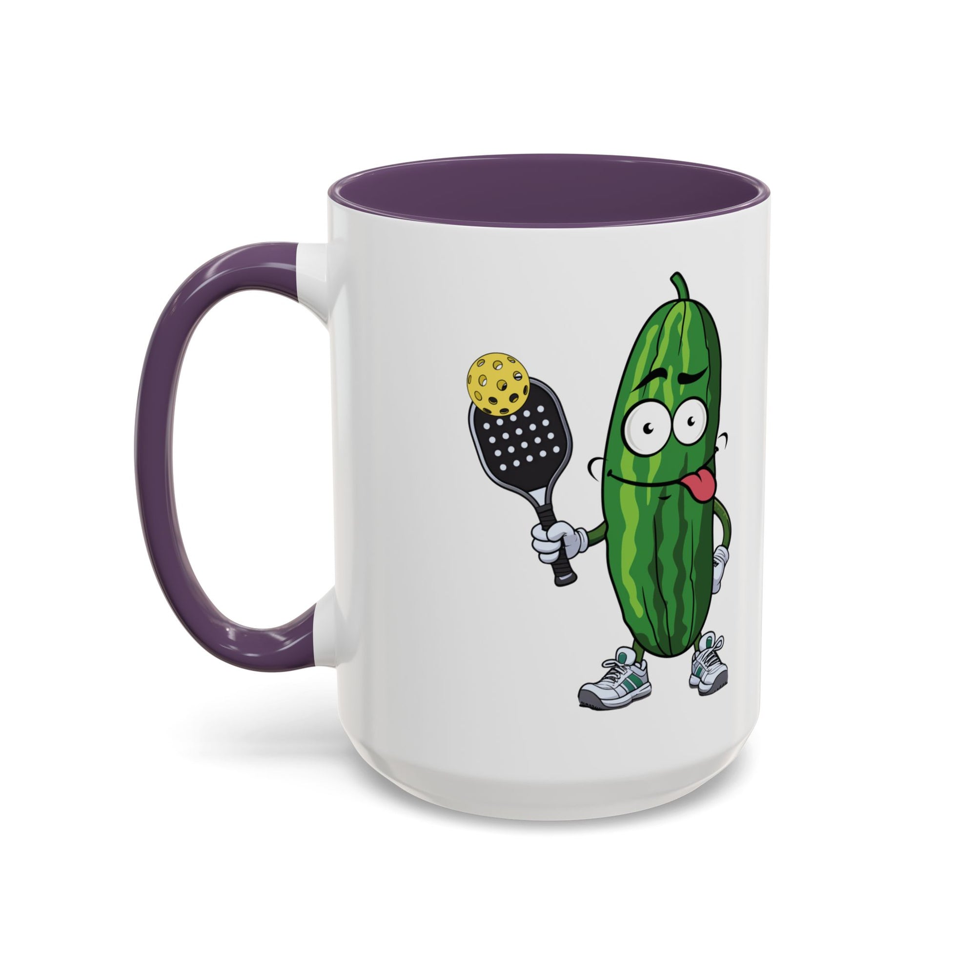 A ceramic coffee mug with purple accents on the handle and interior, with a cartoon pickle with googly eyes and his tongue sticking out, holding a pickleball paddle with a yellow pickleball, against a white background