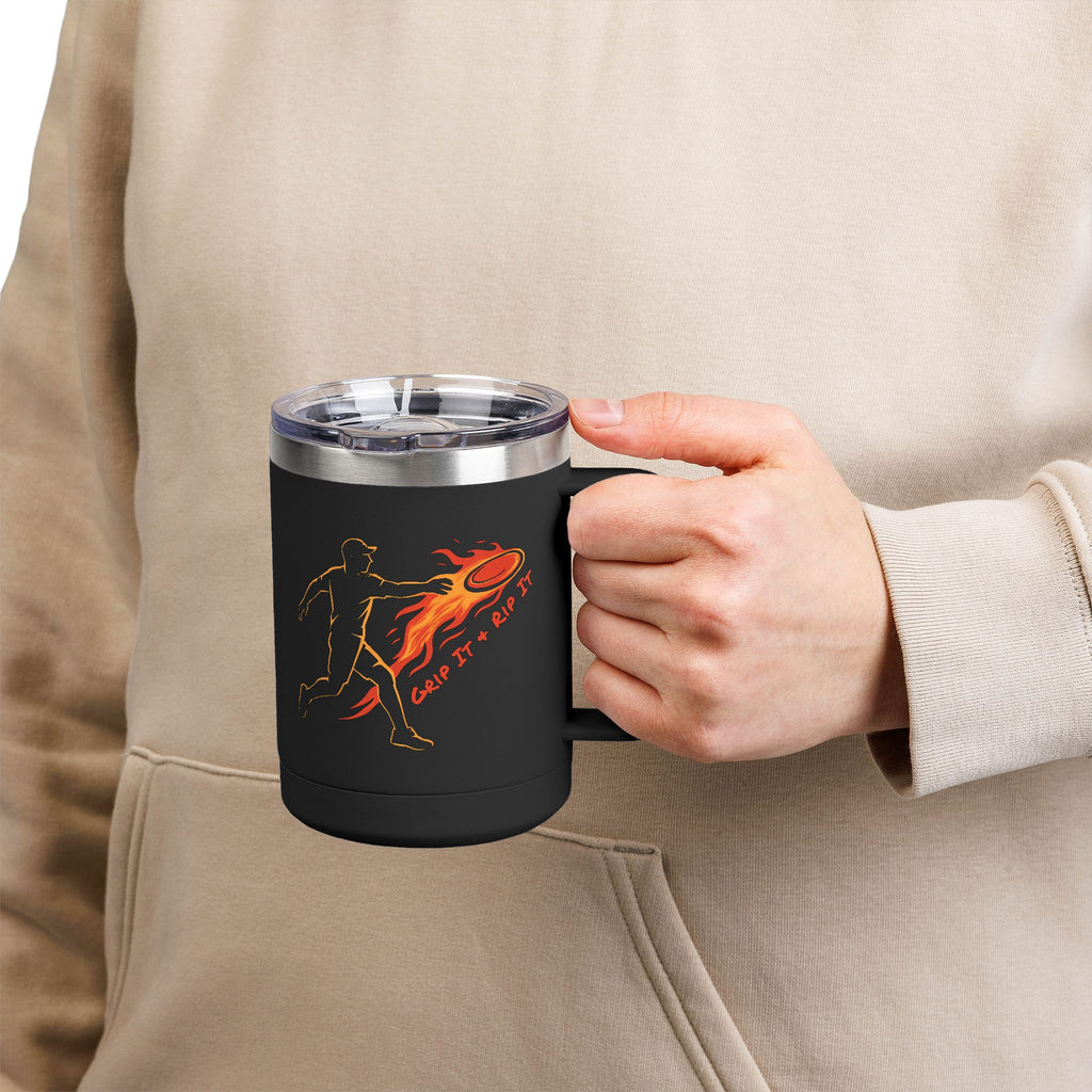 A person holding a black coffee tumbler travel mug with handle and lid featuring a graphic design of a person throwing a disc golf disc with flames coming off the disc and text 'Grip It or Rip It'