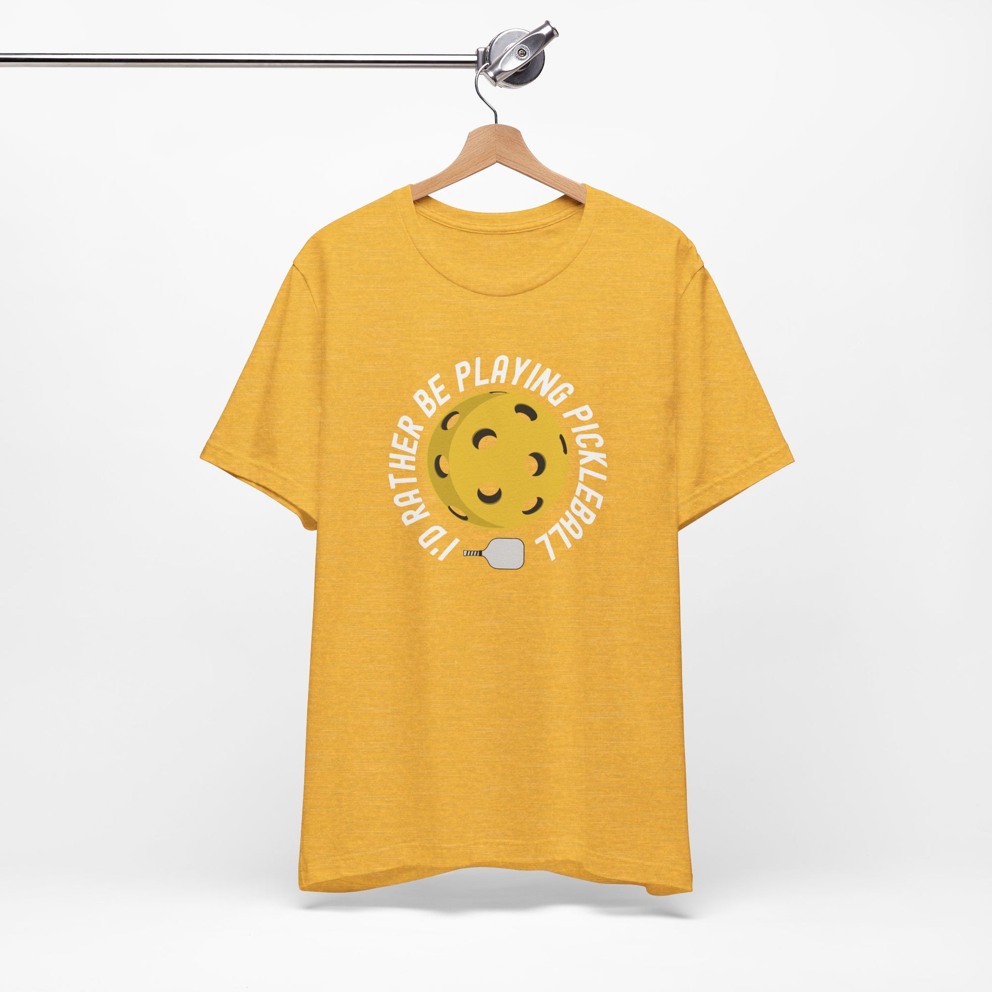 Yellow t-shirt with a yellow pickleball and white pickleball paddle and the text "I'd Rather Be Playing Pickleball" on a hanger against a white background