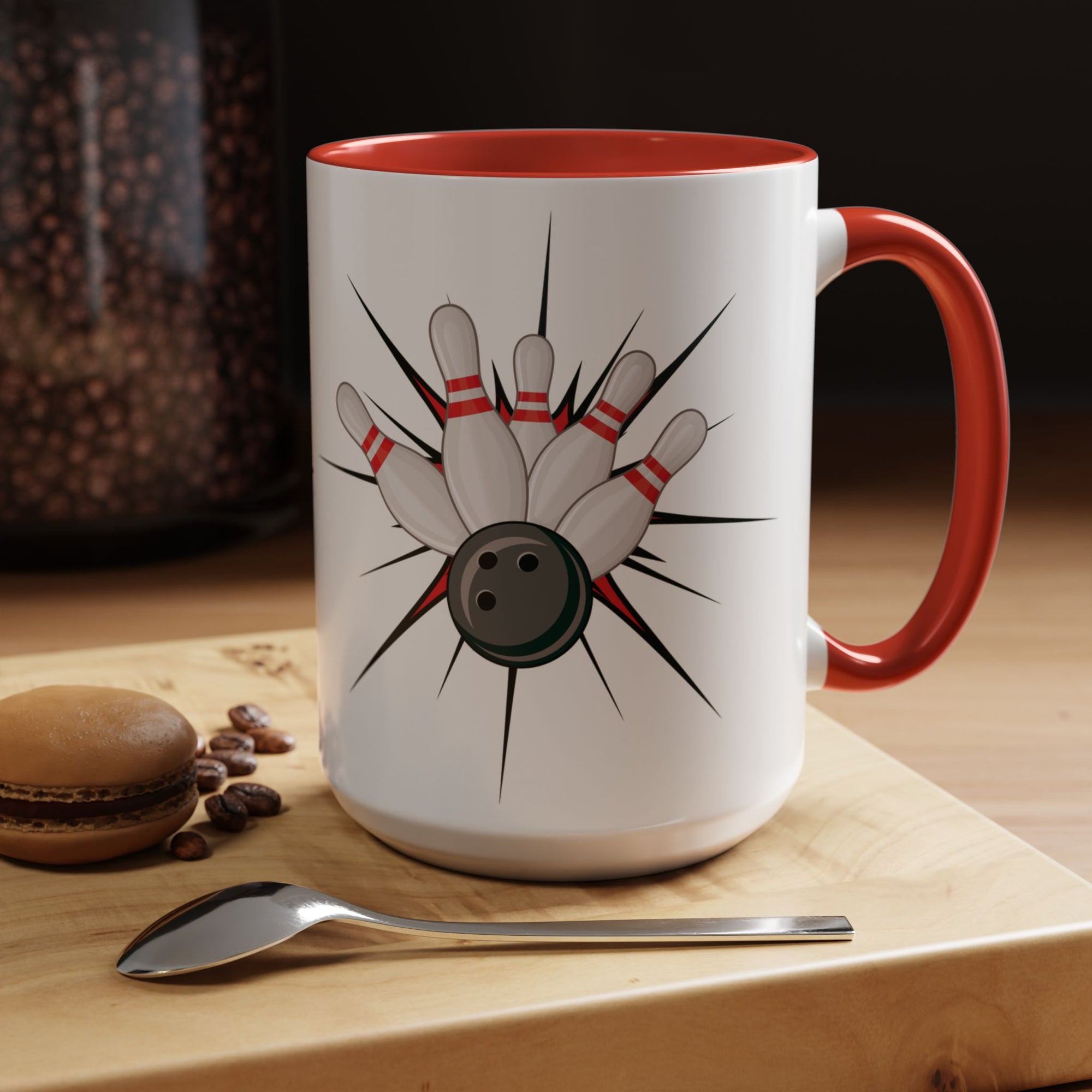 A white ceramic coffee mug with red accents on the handle and interior, with a graphic design of a bowling ball smashing into pins in a coffee shop setting