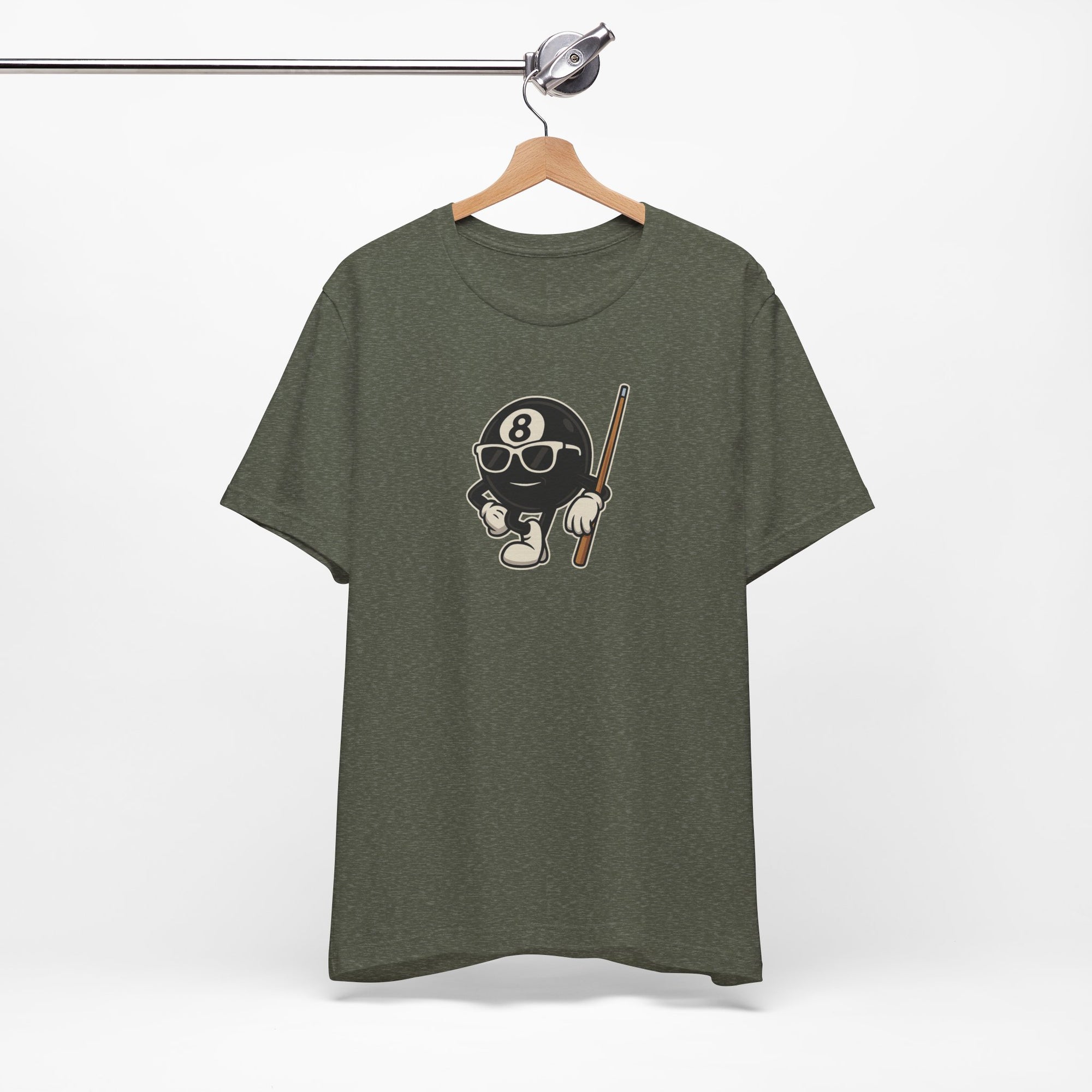 Military green t-shirt with a graphic of a cartoon billiards 8 ball with arms and legs and wearing sunglasses and leaning on a cue stick, on a hanger against a white background