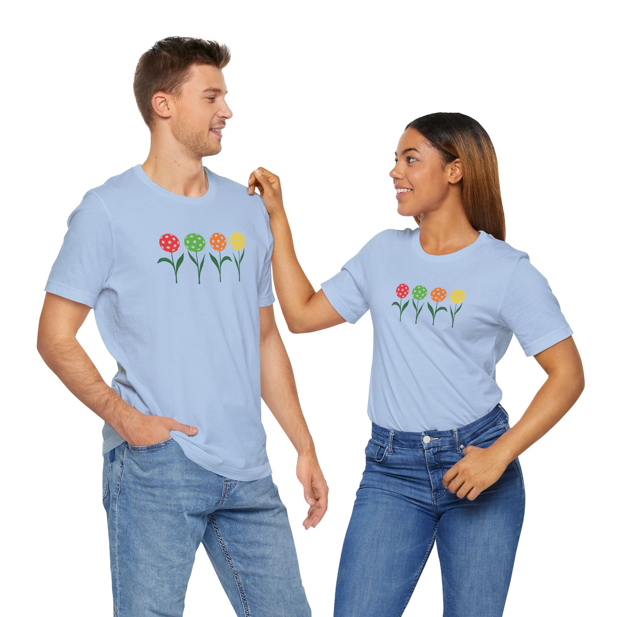 A man and a woman both wearing a light blue t-shirt with colorful flowers made from pickleballs on green stems with leaves, on a hanger against a white background