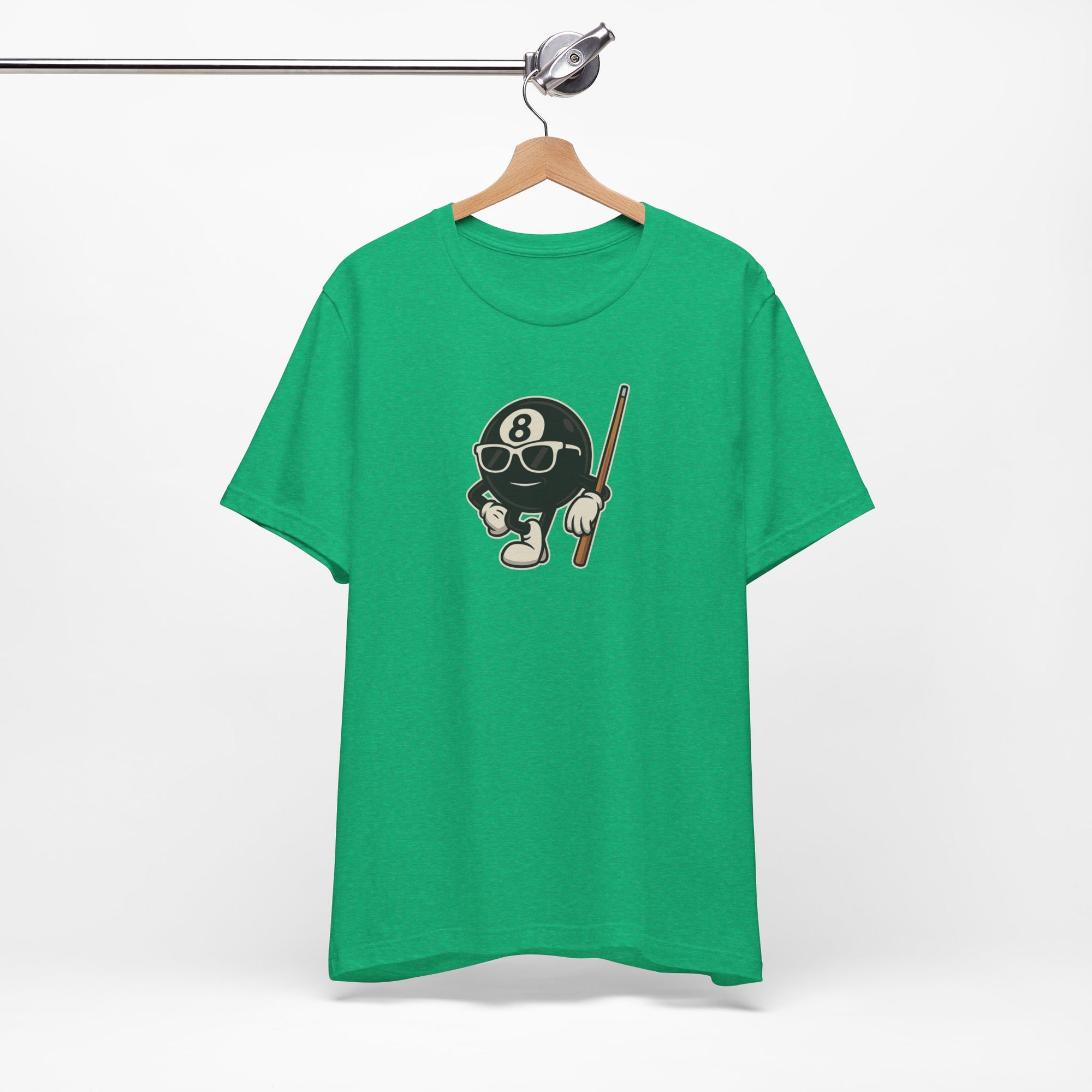 Green t-shirt with a graphic of a cartoon billiards 8 ball with arms and legs and wearing sunglasses and leaning on a cue stick, on a hanger against a white background