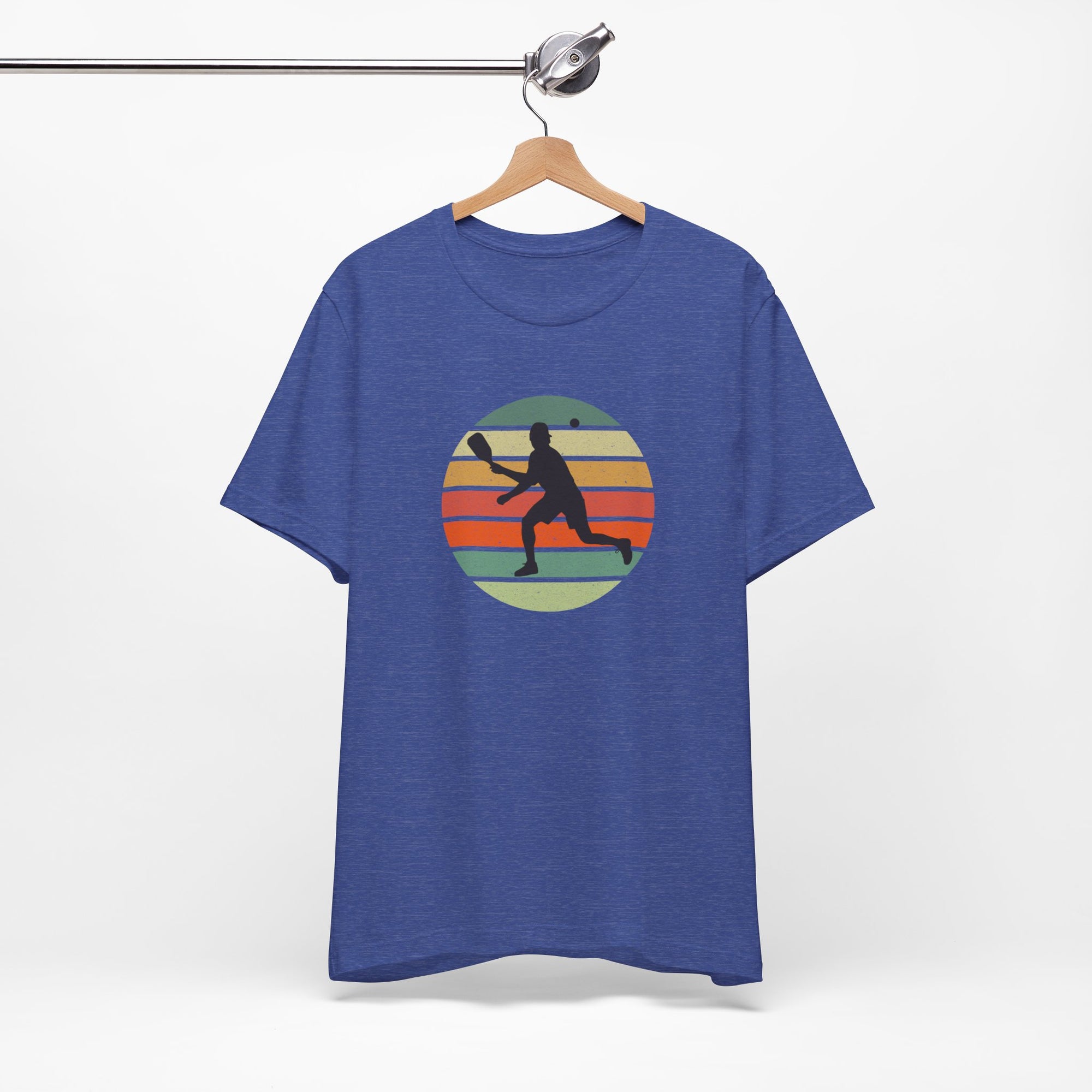 Blue t-shirt with a colorful graphic of a person playing pickleball over a retro colorful circle on a hanger against a white background