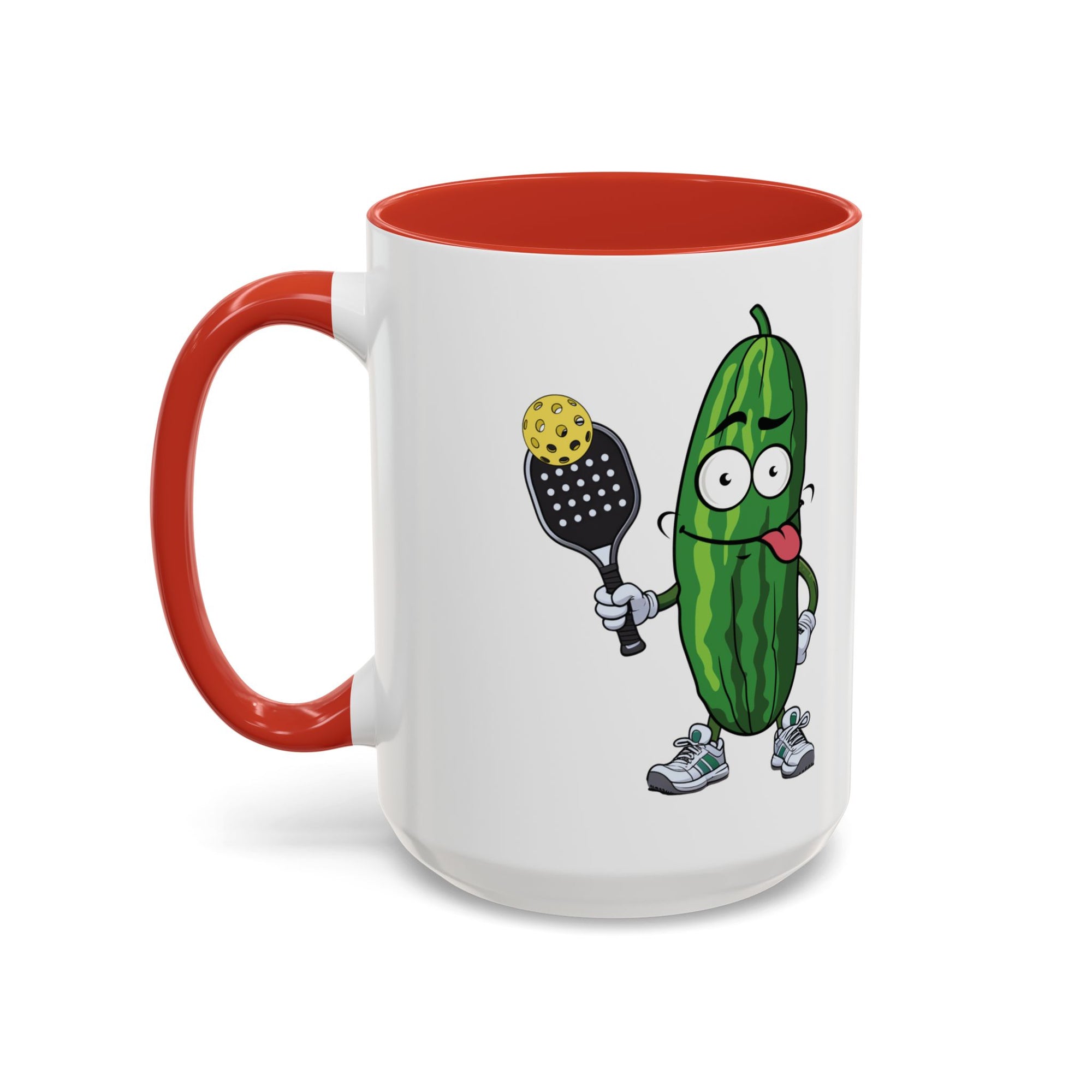 A ceramic coffee mug with red accents on the handle and interior, with a cartoon pickle with googly eyes and his tongue sticking out, holding a pickleball paddle with a yellow pickleball, against a white background