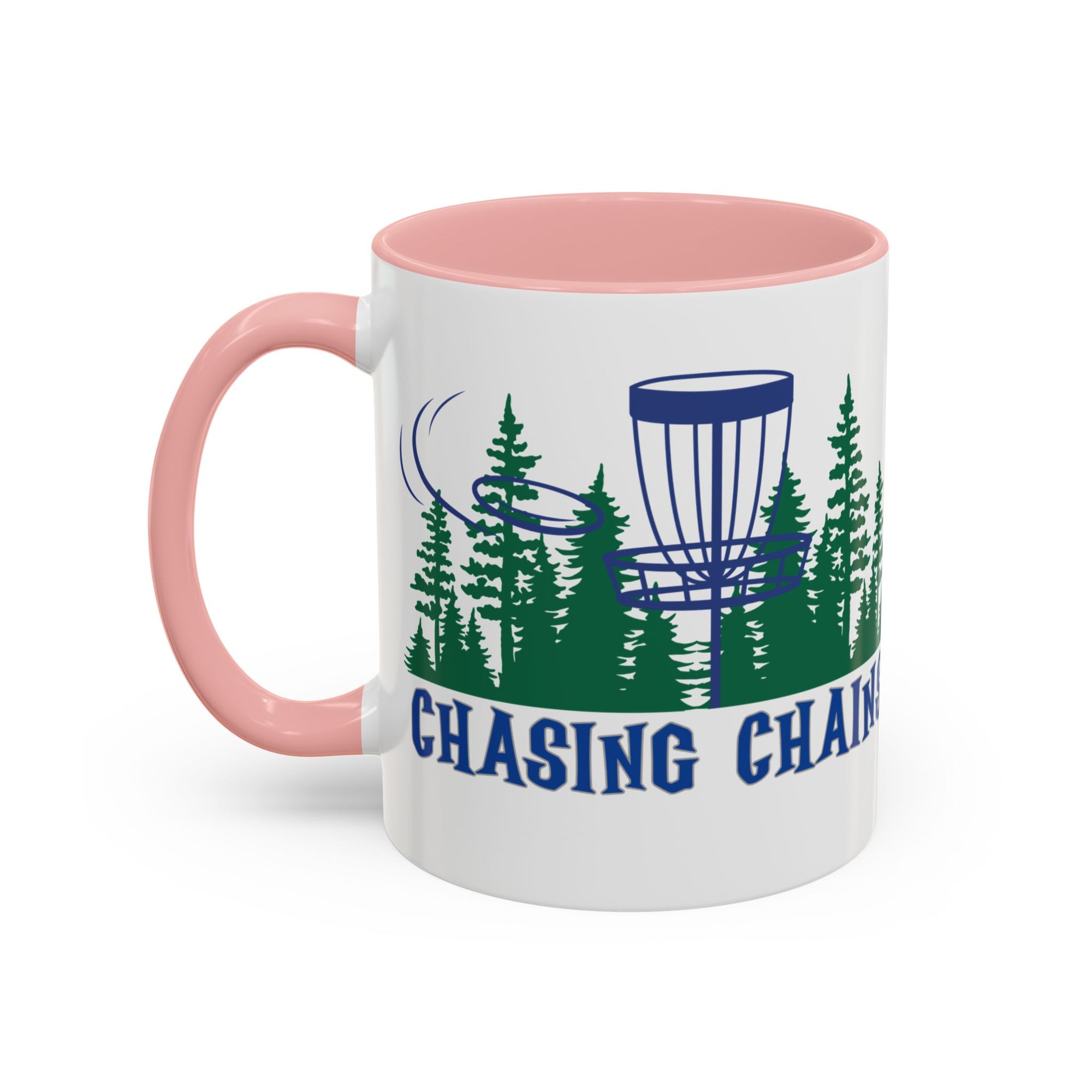 A ceramic coffee mug with pink accents on the handle and interior, with 'Chasing Chains' graphic featuring a flying disc golf disc and basket and chains in front of a scenic evergreen tree landscape, against a white background