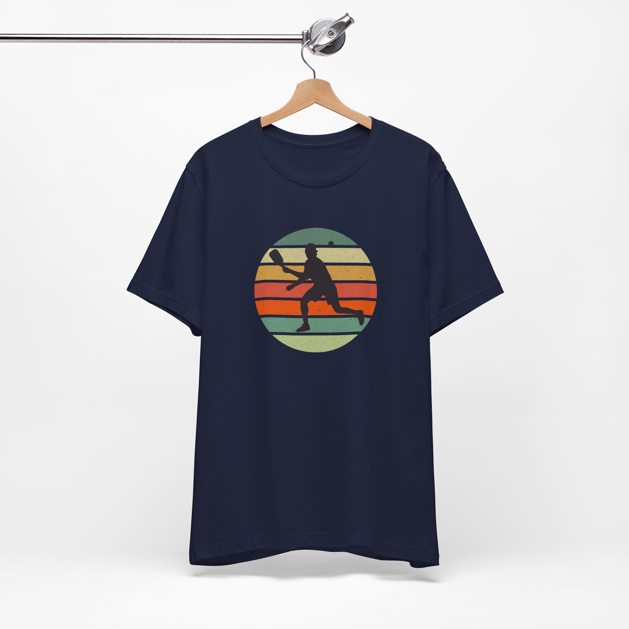 Navy blue t-shirt with a colorful graphic of a person playing pickleball on a hanger against a white background
