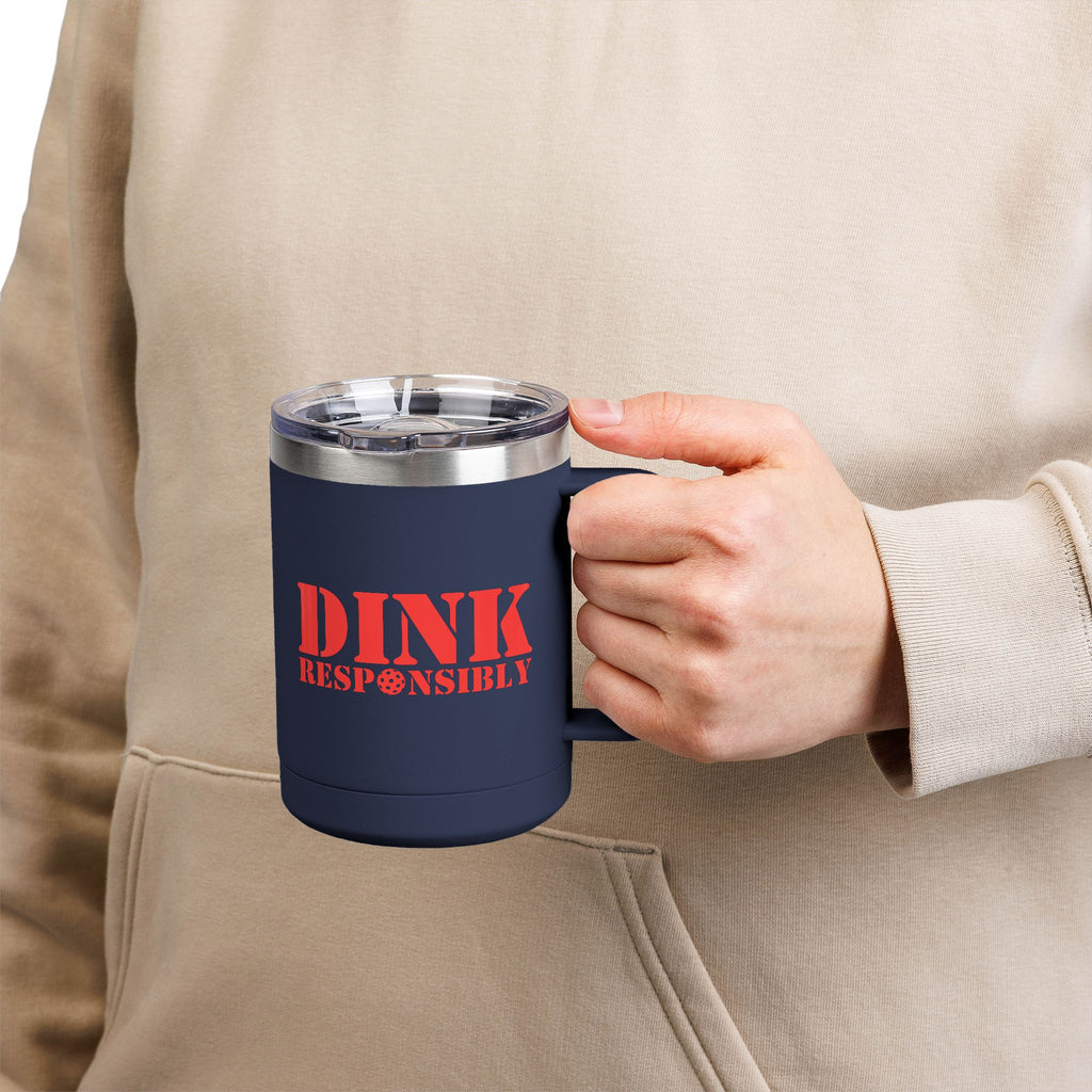 A person holding a blue travel coffee mug  with a handle and lid, with red text 'DINK RESPONSIBLY' with a pickleball replacing the "O" in "Responsibly"