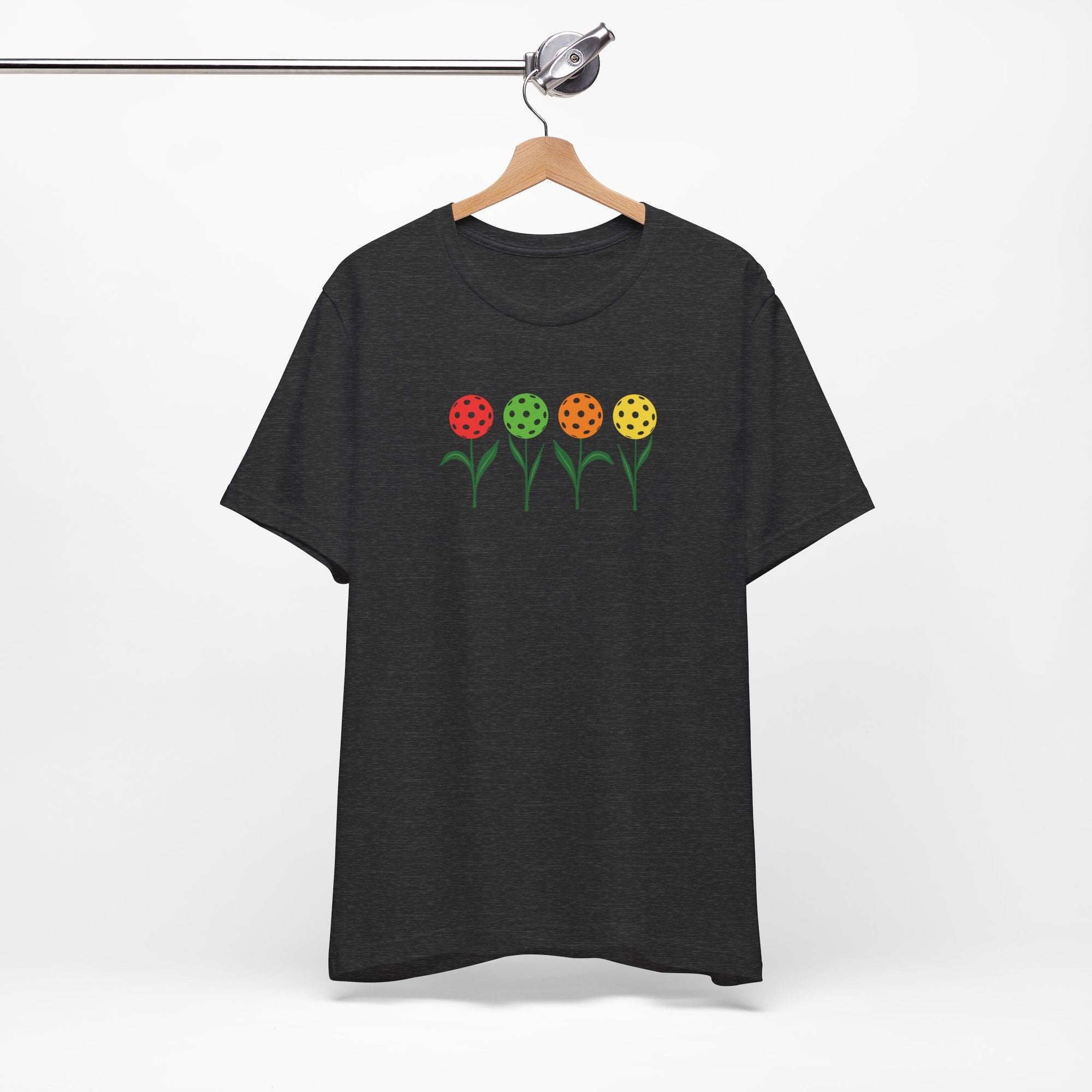 Dark gray t-shirt with colorful flowers made from pickleballs on green stems with leaves, on a hanger against a white background