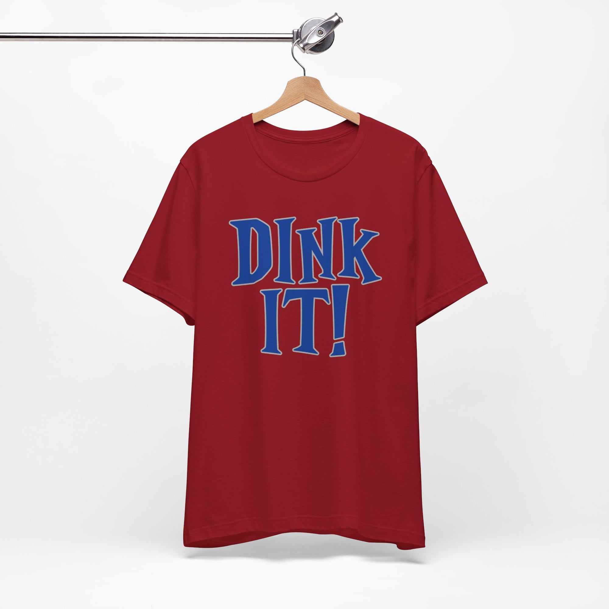 Red t-shirt with 'DINK IT!' text in blue and outlined in gray, on a hanger against a white background