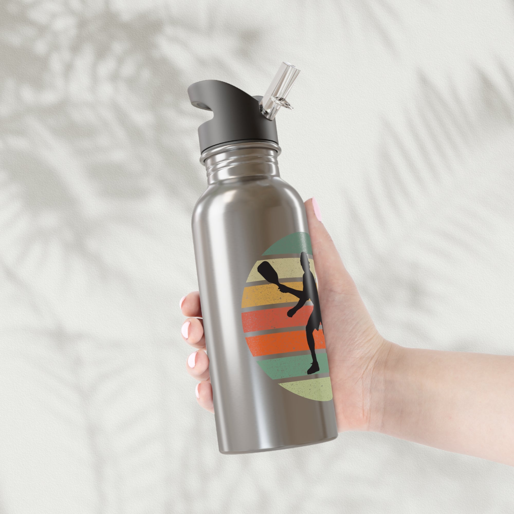 Hand holding a stainless steel water bottle with a graphic of a silhouette of a pickleball player over a retro colorful background on a light gray background