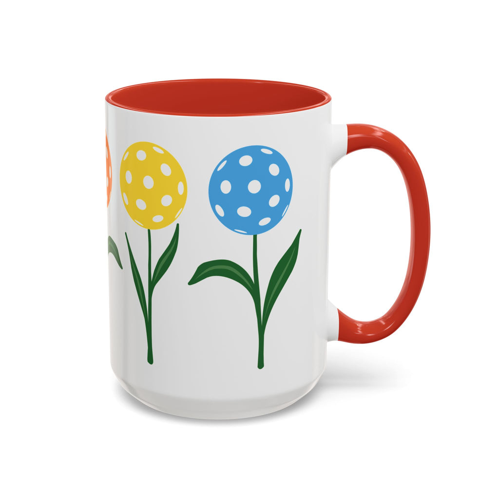 A ceramic coffee mug with red accents on the handle and interior, with colorful flowers made from pickleballs on green stems with leaves, against a white background