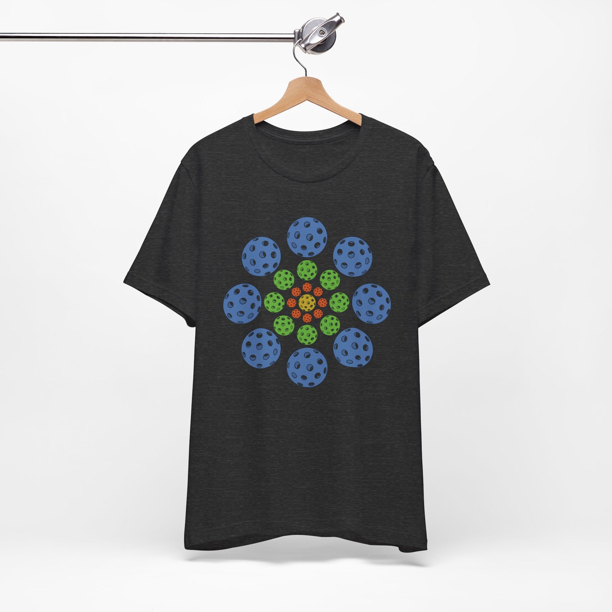 Dark gray t-shirt with colorful geometric design of pickleballs on a hanger against a white background