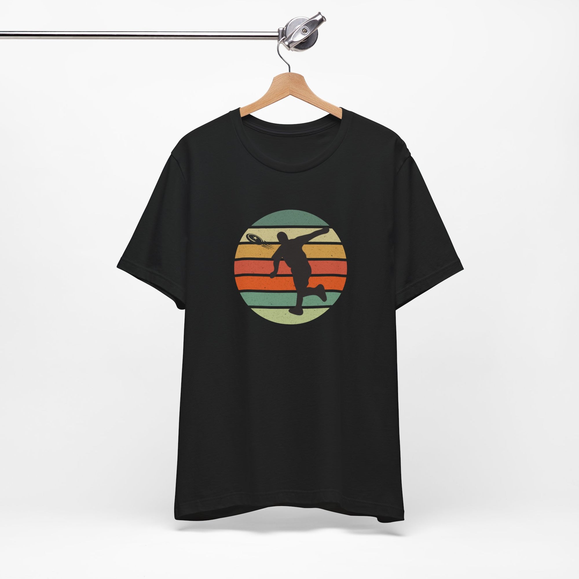 Black t-shirt with a graphic of a silhouette disc golf player throwing a disc above a colorful retro graphic, hanging on a wooden hanger.