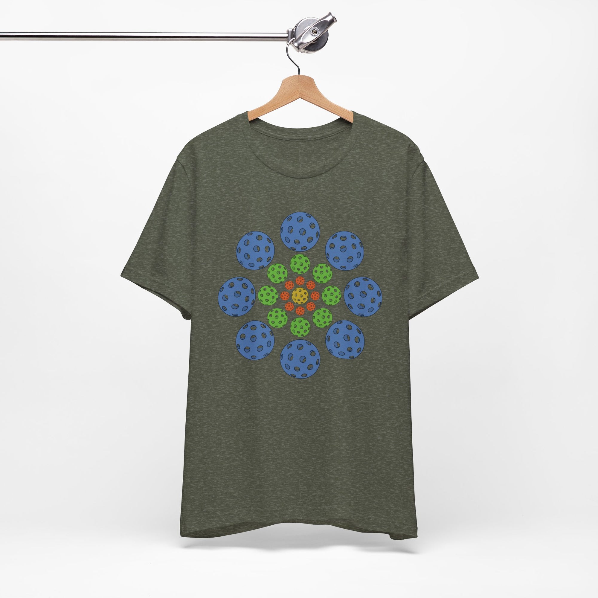 Military green t-shirt with colorful geometric design of pickleballs on a hanger against a white background