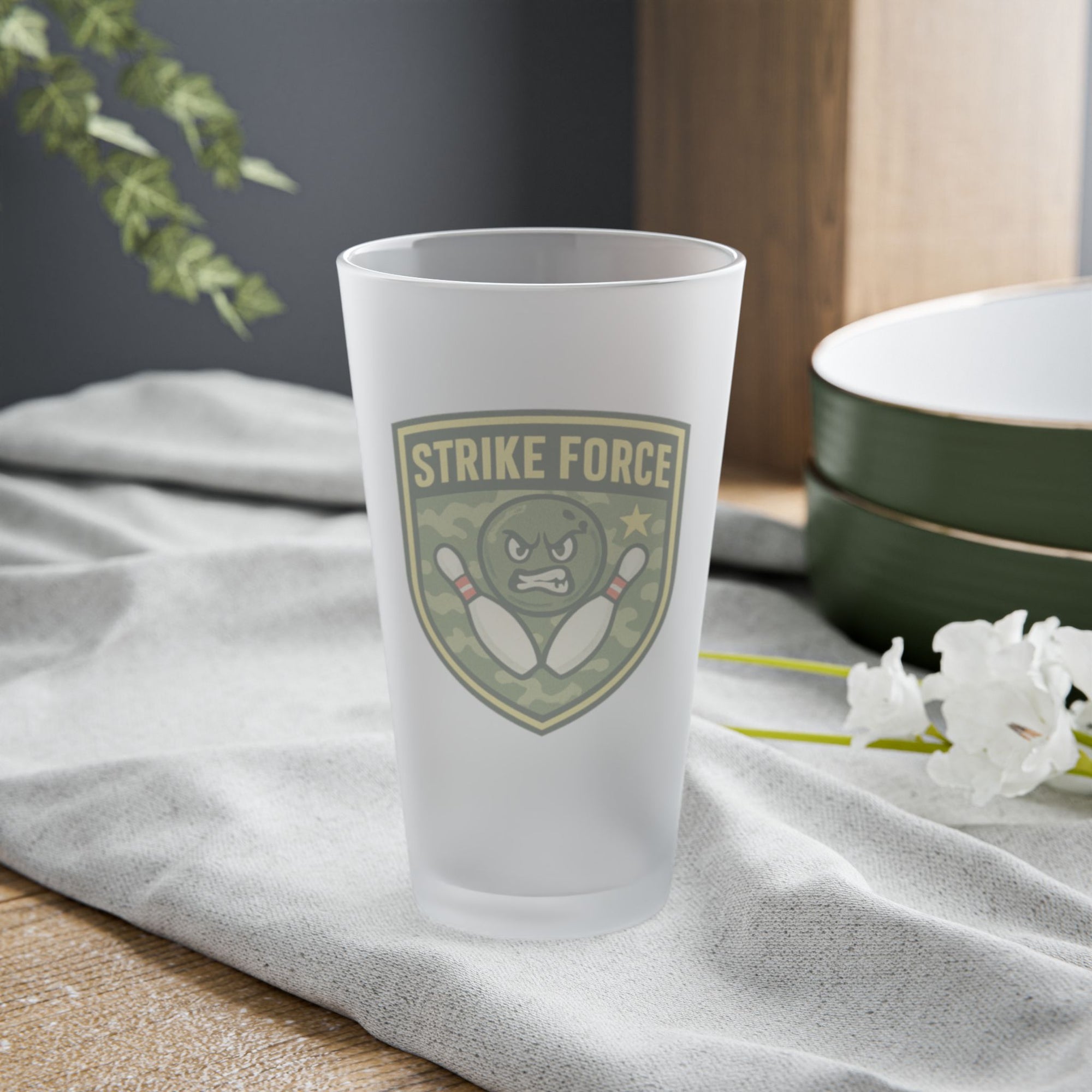 Frosted pint glass with bowling 'Strike Force' military-style patch on a tabletop