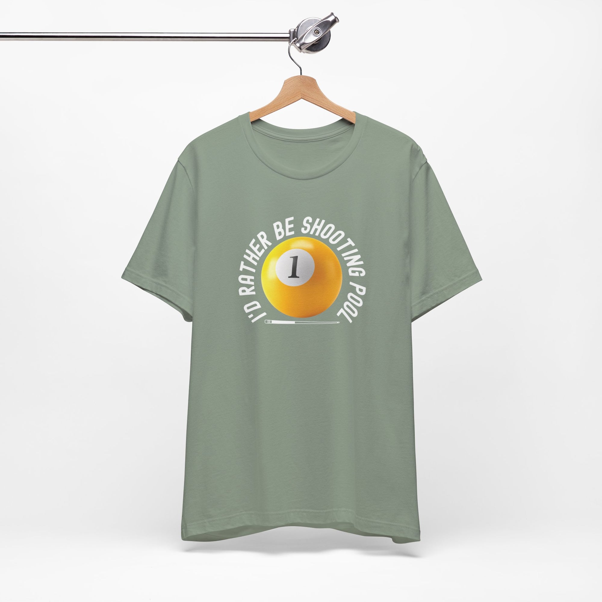 Light green t-shirt with a yellow billiards ball and cue stick graphic and the text "I'd Rather Be Shooting Pool" on a hanger against a white background