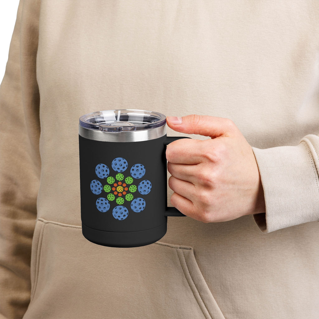 A person holding a black travel mug with lid and handle featuring a colorful geometric design of pickleballs